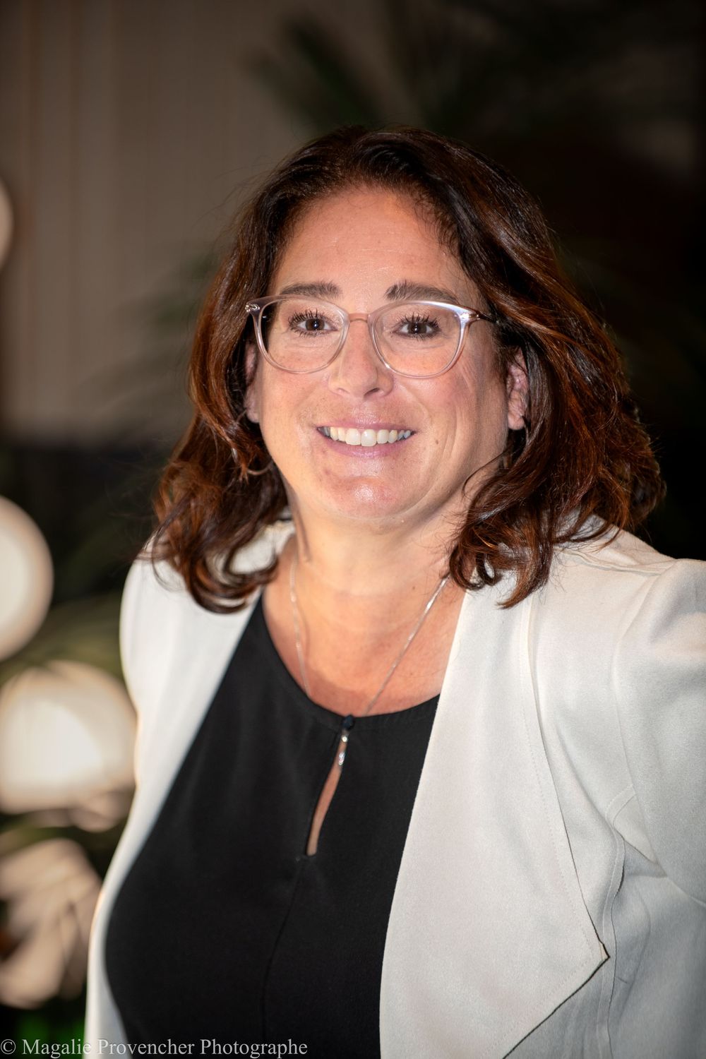 A person wearing glasses and a white blazer smiles warmly while posing for a series of headshots.