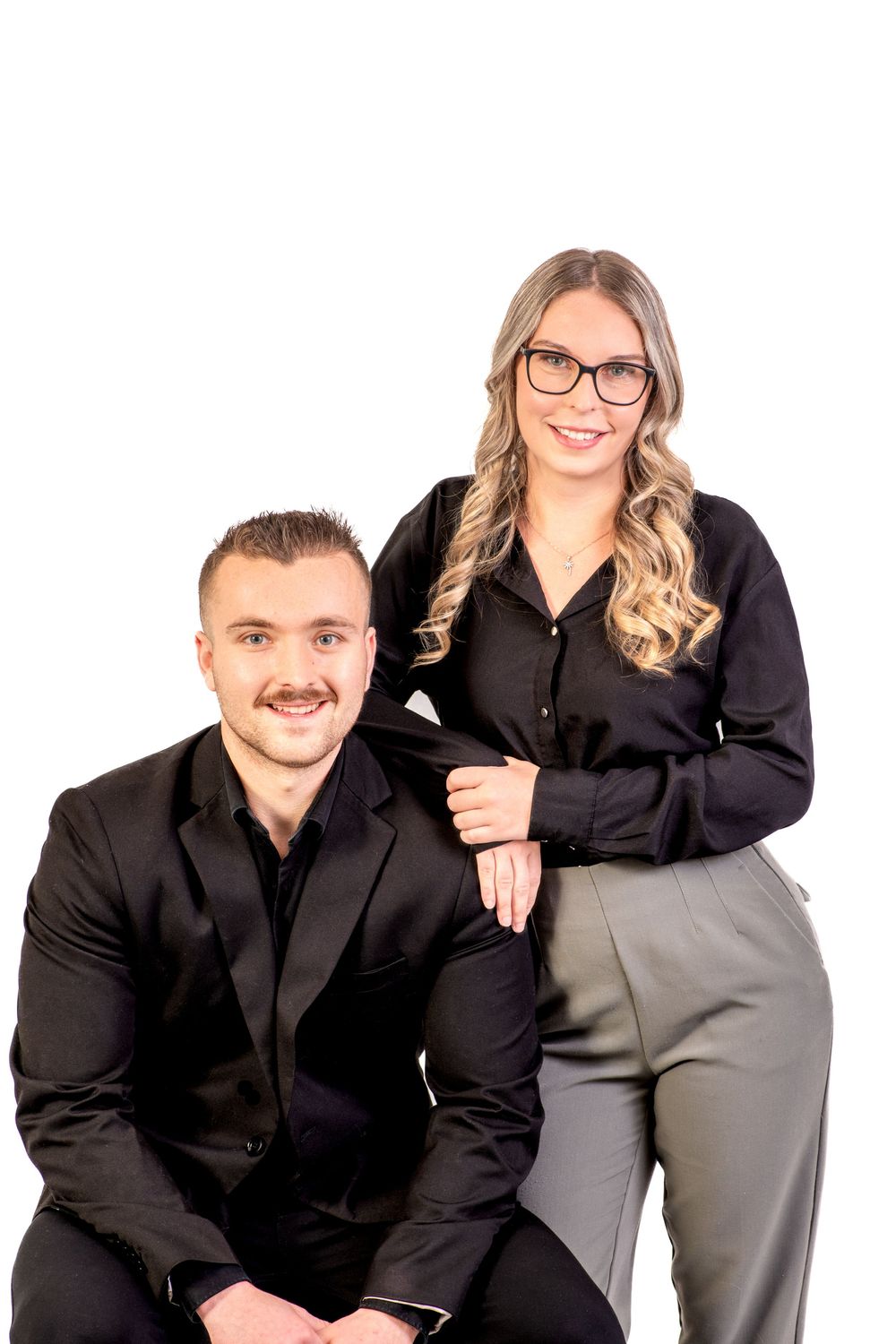 Professional business team in coordinated black attire poses together for corporate portrait against white background.