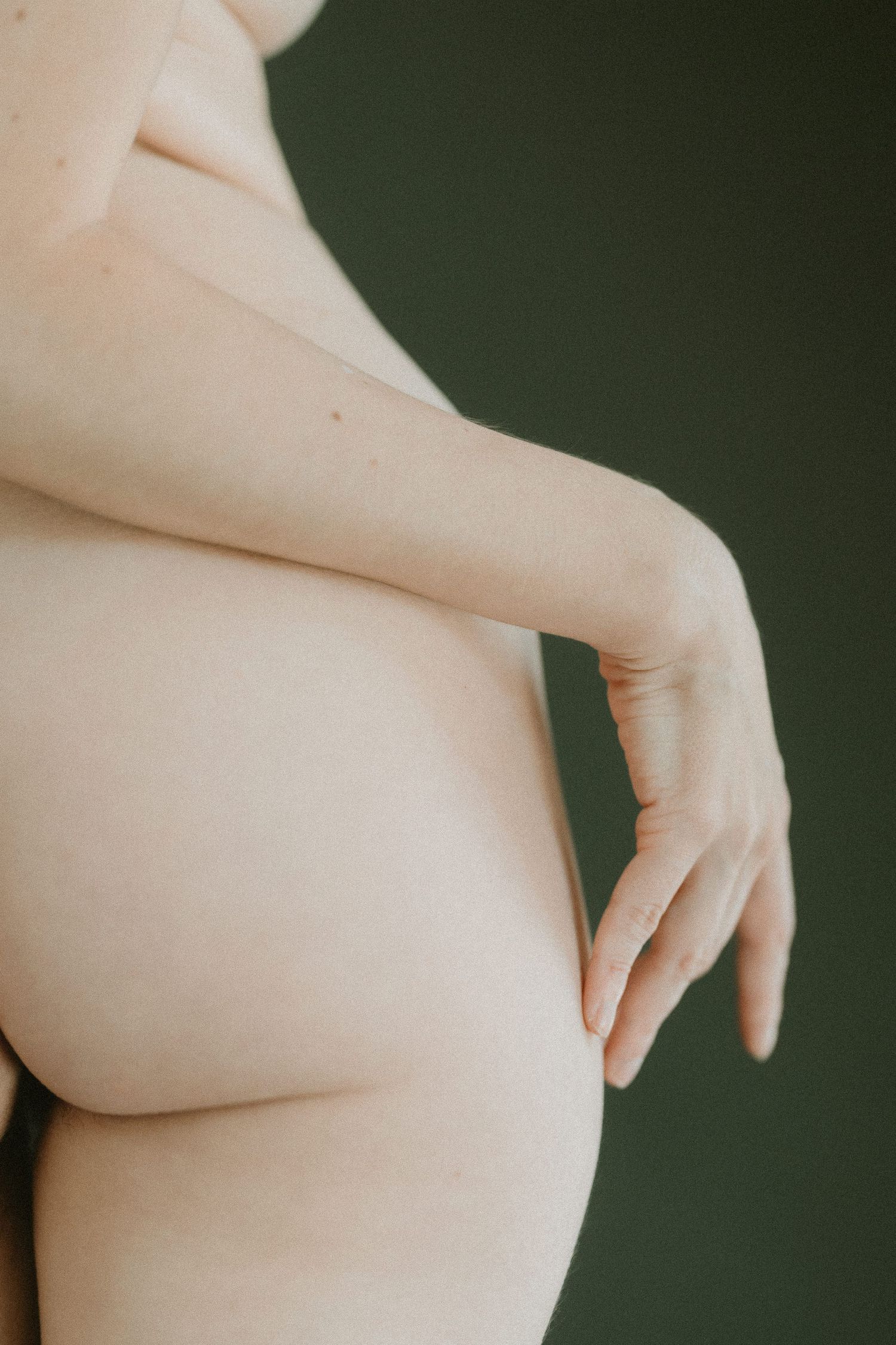 Minimalist close-up nude study focusing on curves and form against dark background.
