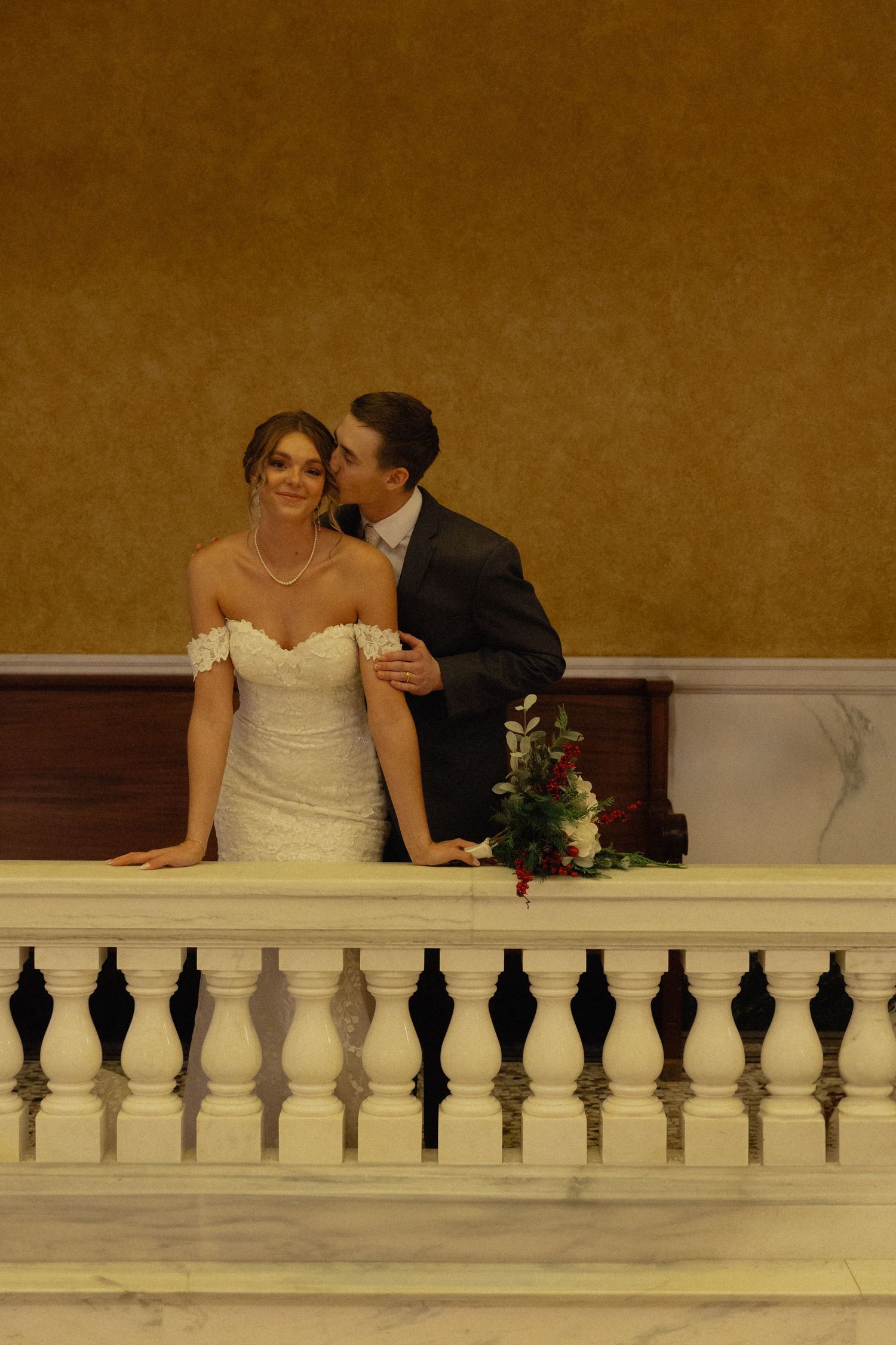 Newlywed couple sitting behind ornate white balustrade railing at their wedding venue.