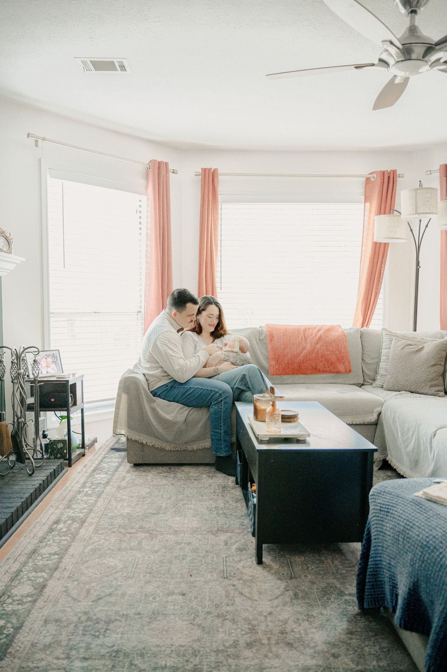 Couple relaxes together on sectional sofa in bright living room with coral curtains.