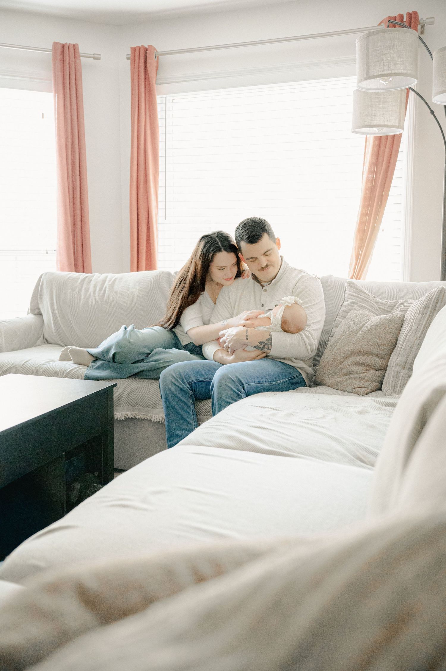 Family cuddles together on white sectional sofa in modern living room.