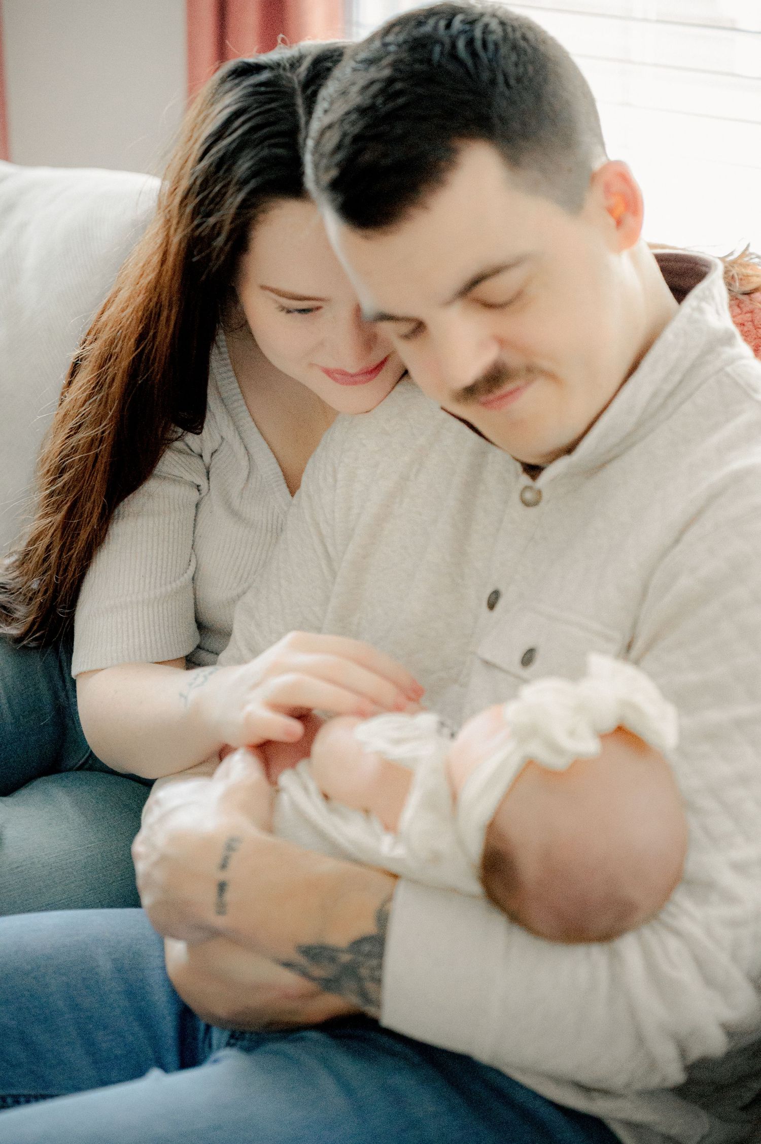 Parents share tender moment with newborn baby on grey couch.