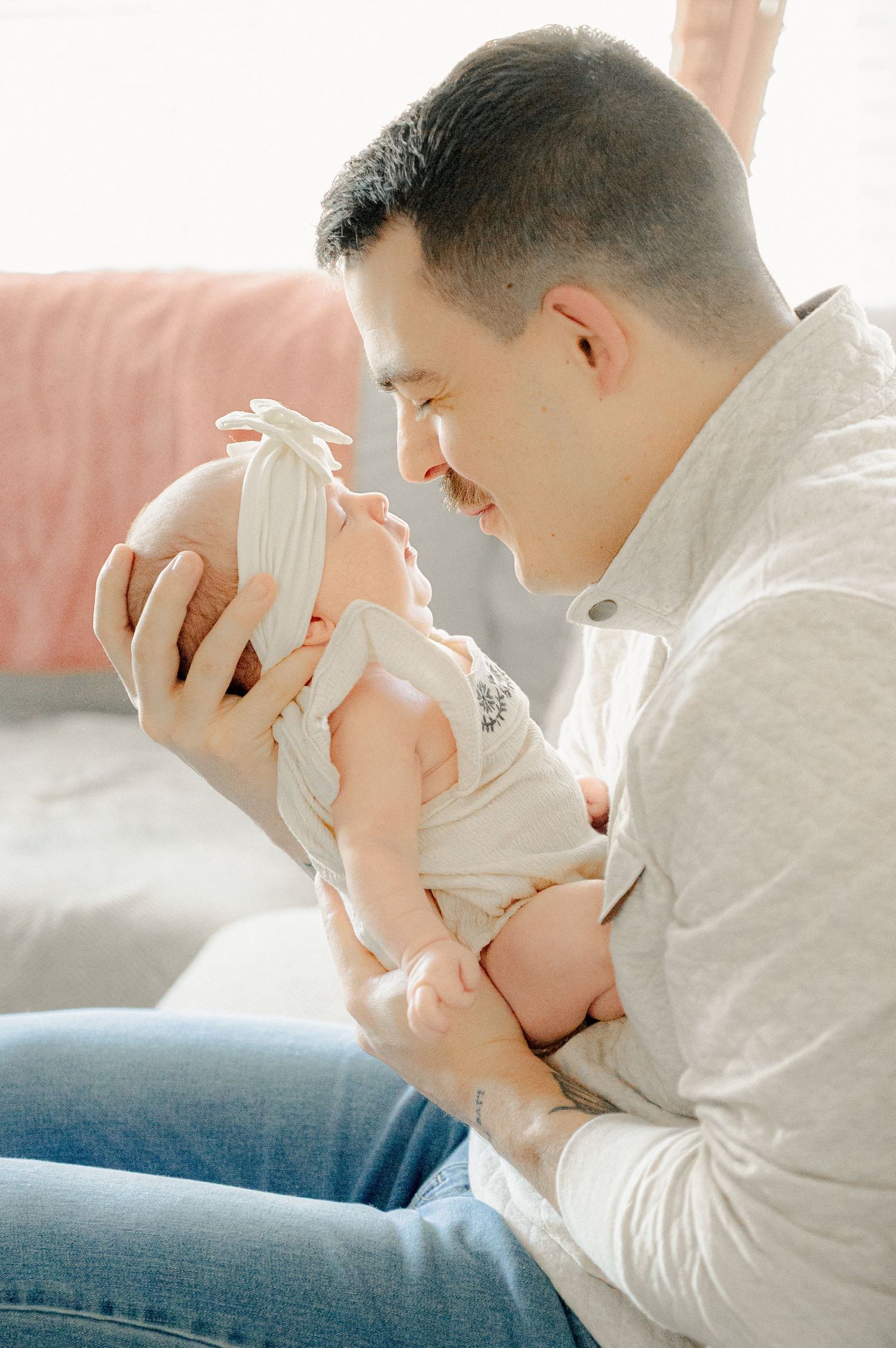 Parent holding newborn baby in white onesie on grey sofa.