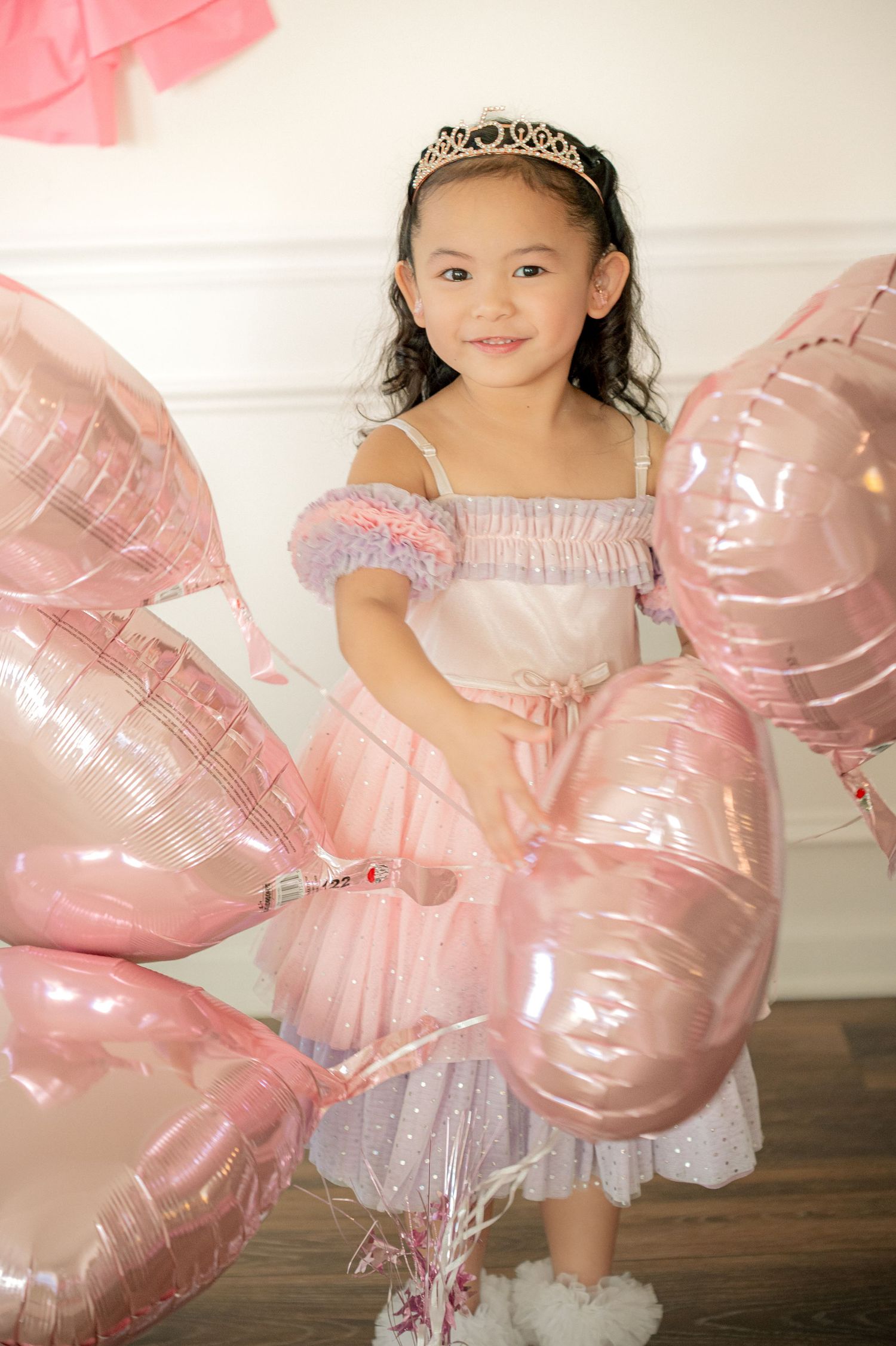 A whimsical birthday photoshoot with pink heart balloons and tulle dress.