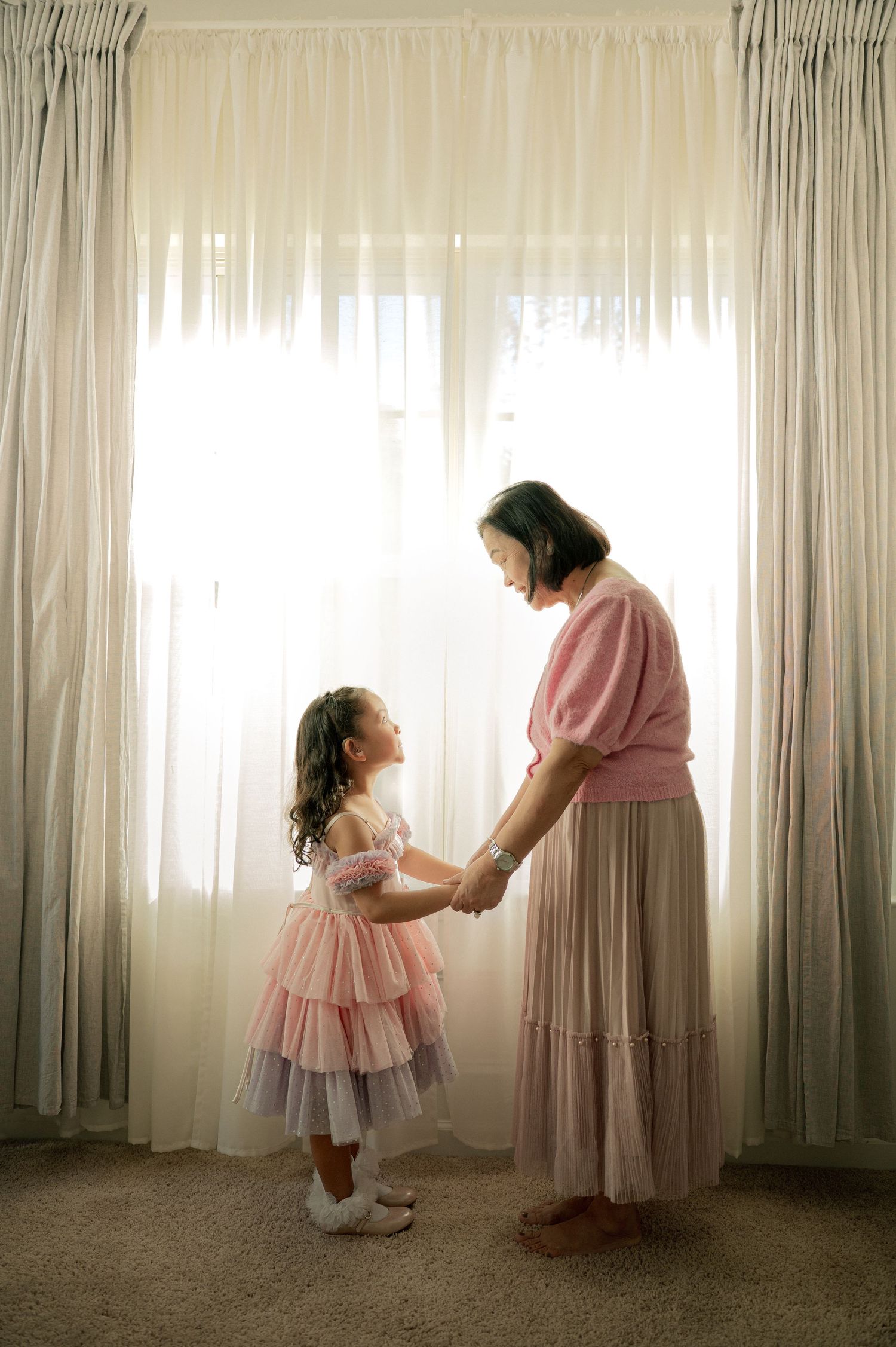 A touching scene of two figures in pink dresses sharing a tender moment by a window.