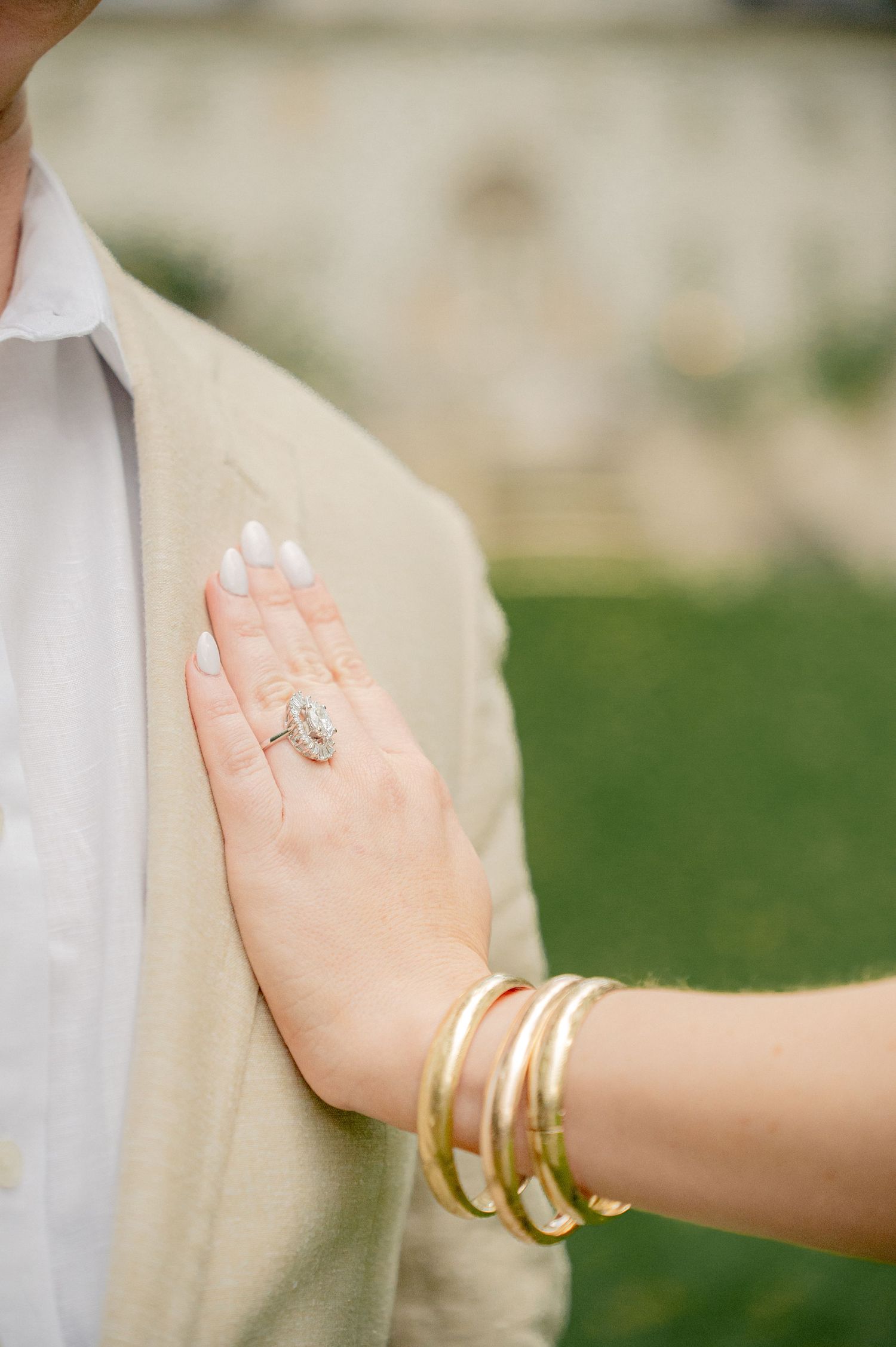 Close-up of hands wearing gold bangles and engagement ring against light background.