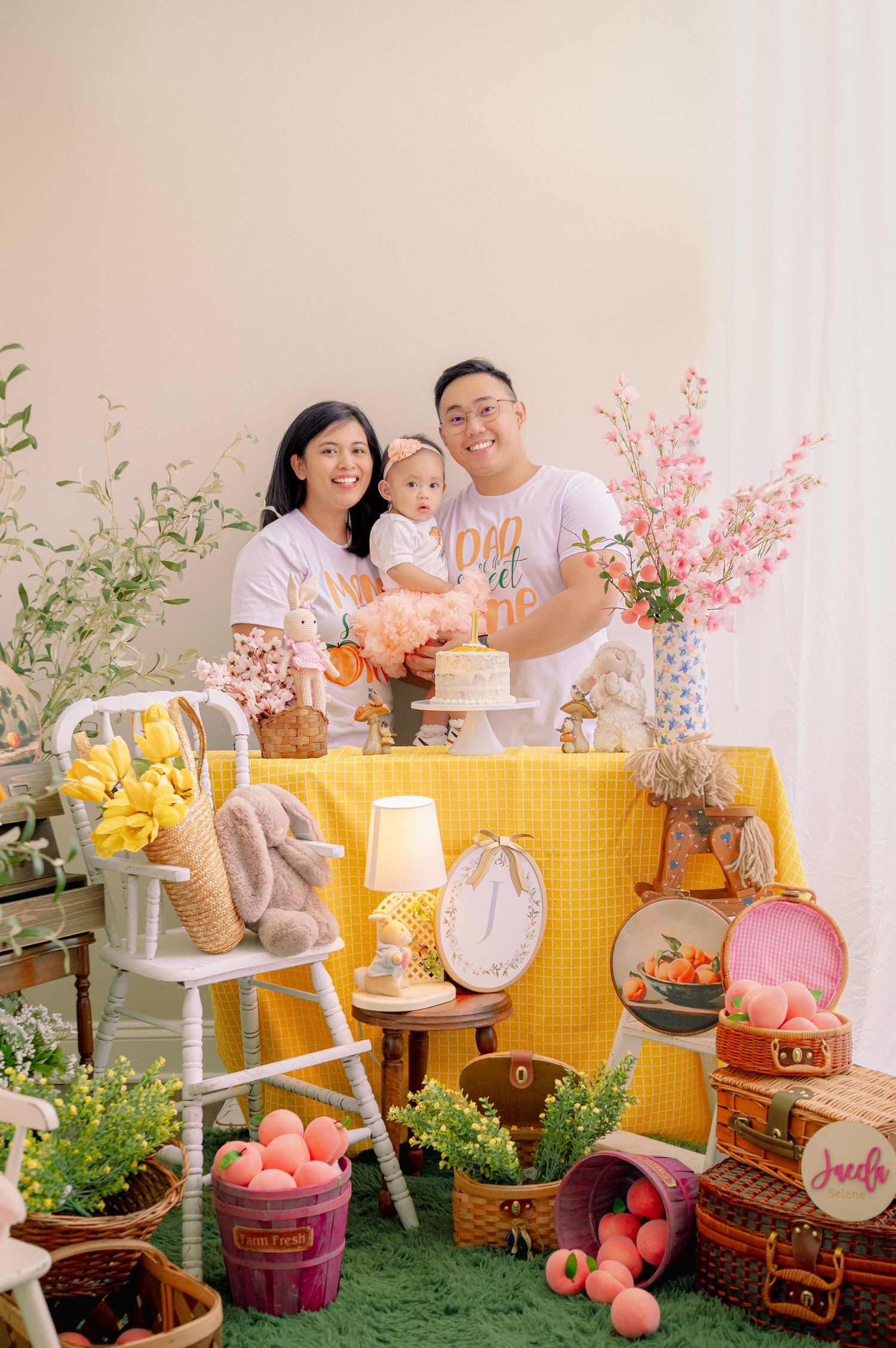 Festive pink and yellow party setup with floral decorations, plush toys, and a gingham backdrop.