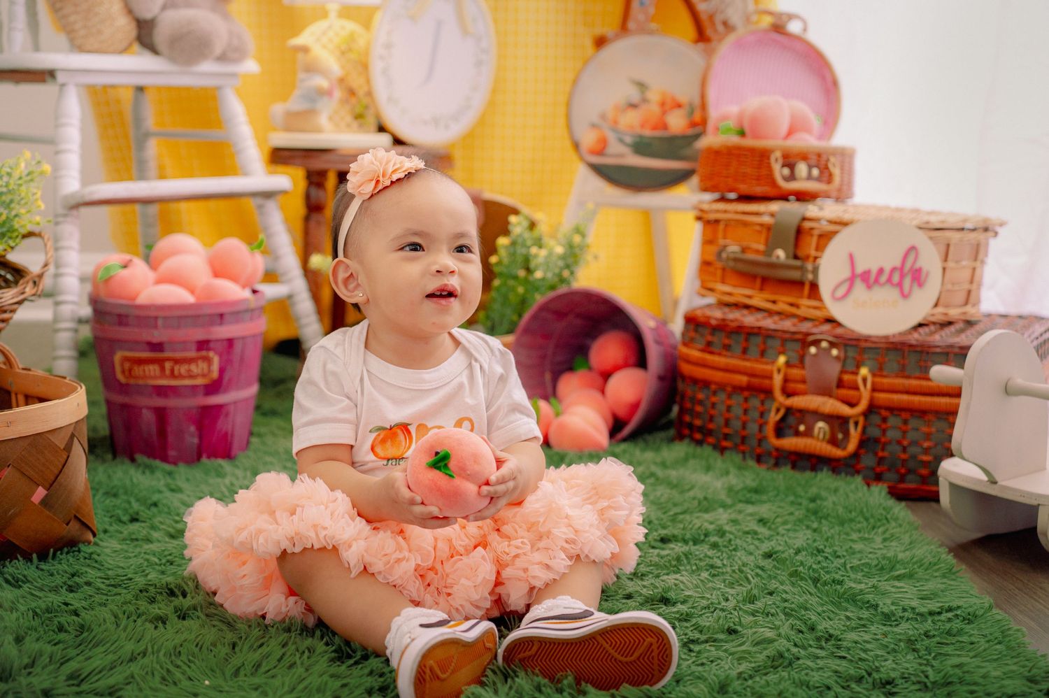 Baby wearing peach tutu outfit sitting among party decorations and toys.