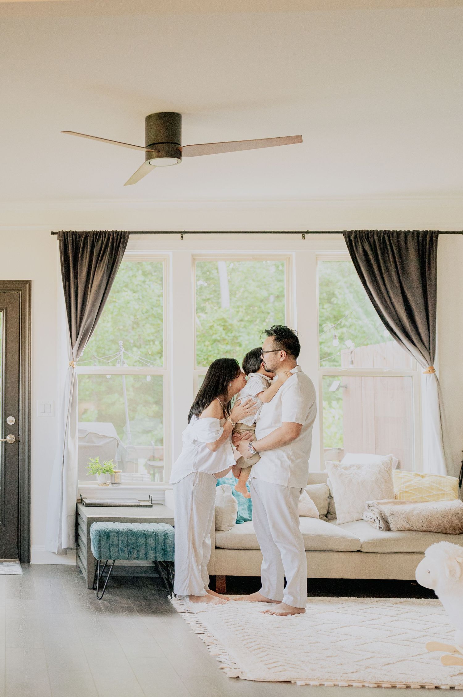 Family shares tender moments in bright, minimalist living room with large windows.