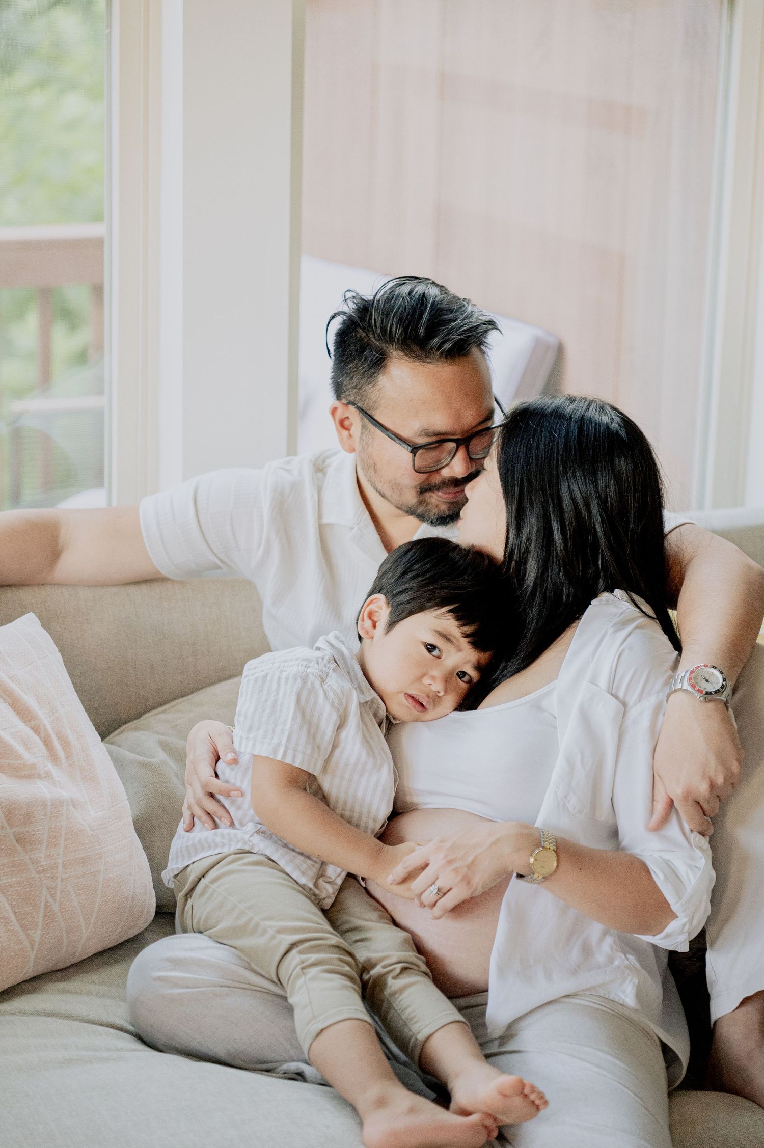 Couple shares intimate moment on beige couch during maternity session.