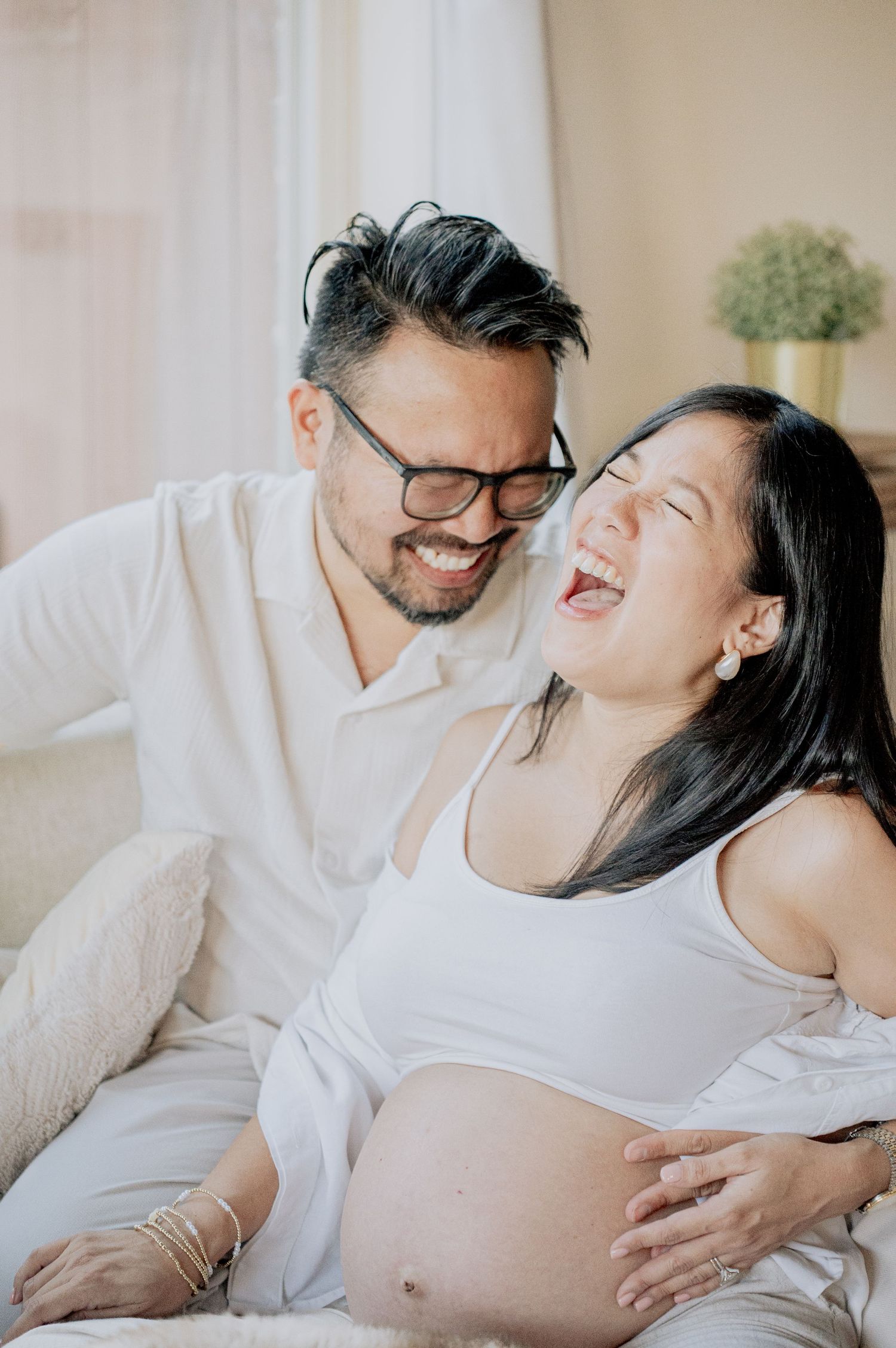 Joyful maternity photo session with couple laughing on couch.