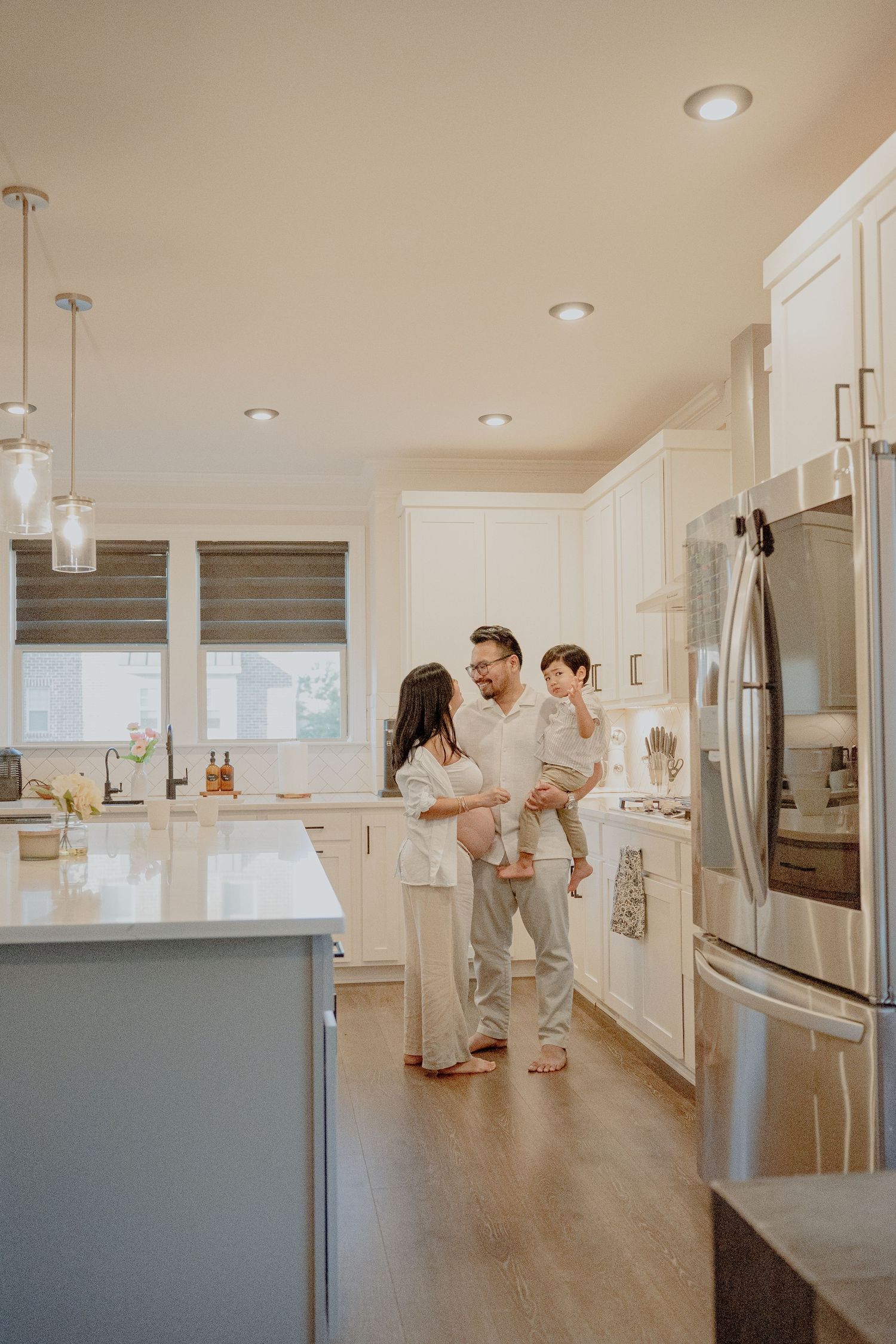 Playful couple dances in modern white kitchen during maternity photoshoot.