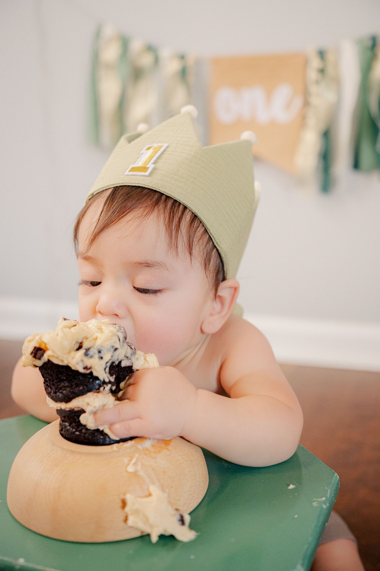 Baby wearing paper crown eating cake with messy face and frosting.