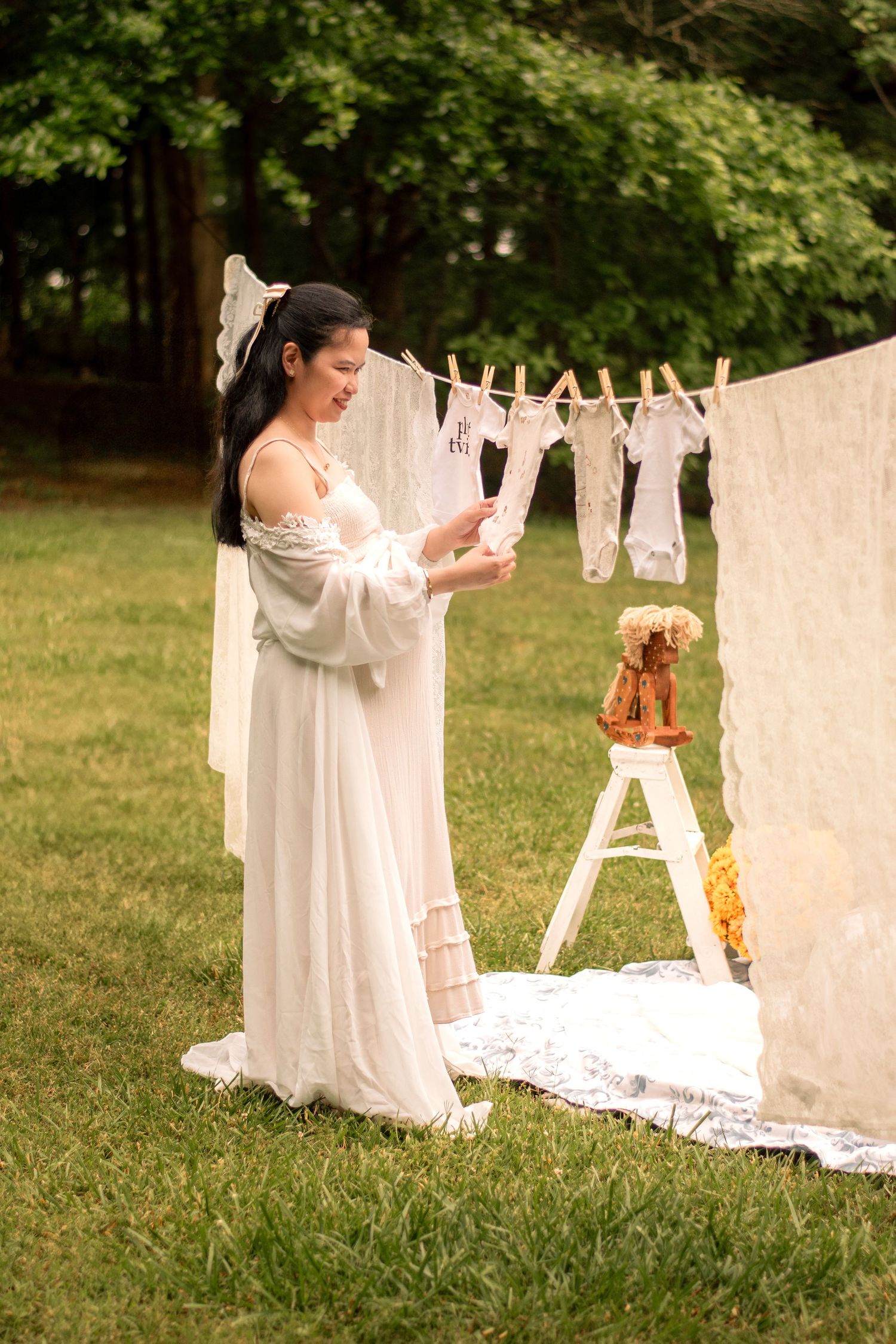 Outdoor maternity photoshoot with white linens hanging on clotheslines in a green garden setting.