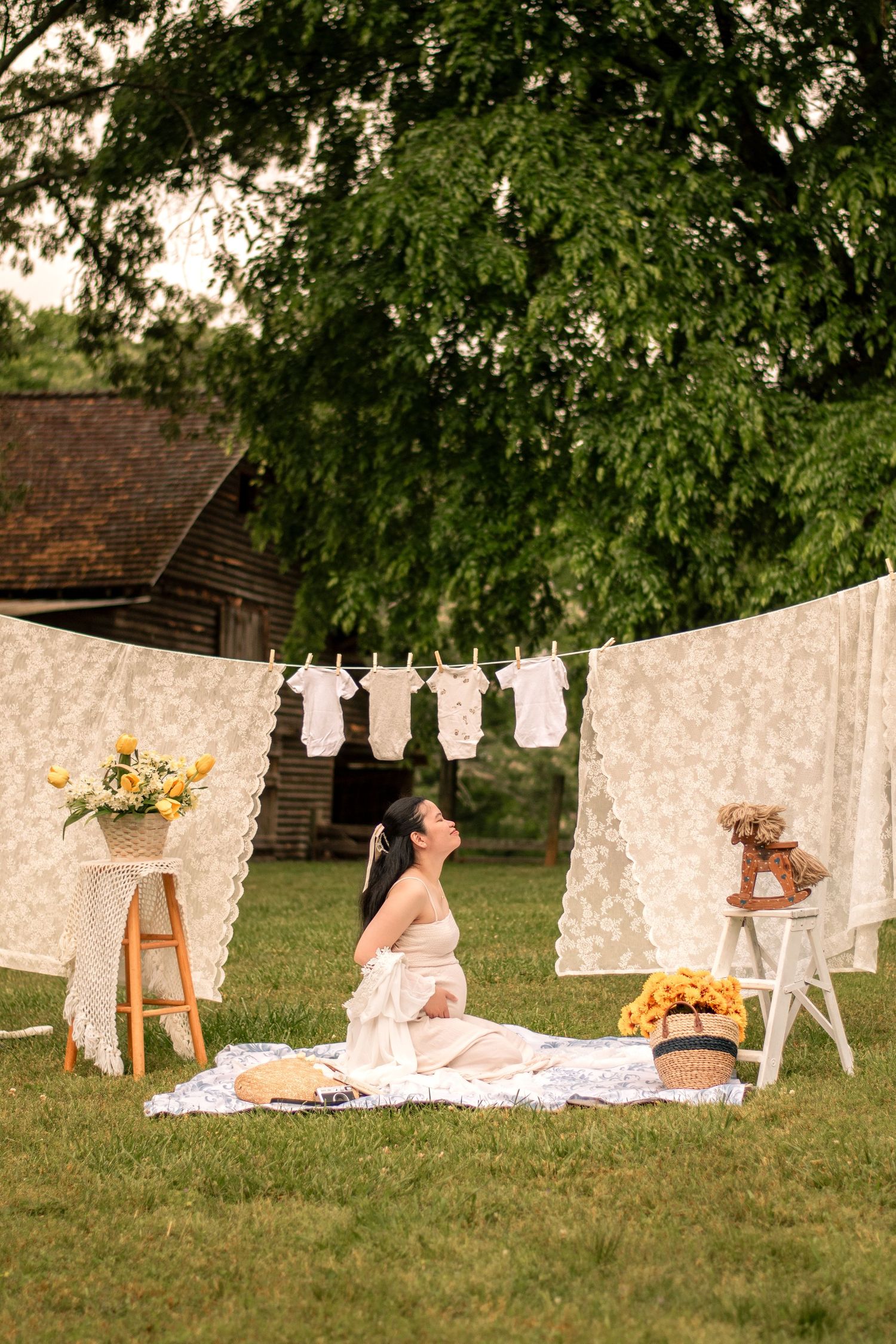 Artistic maternity session in a garden with vintage white linens and decorative elements.