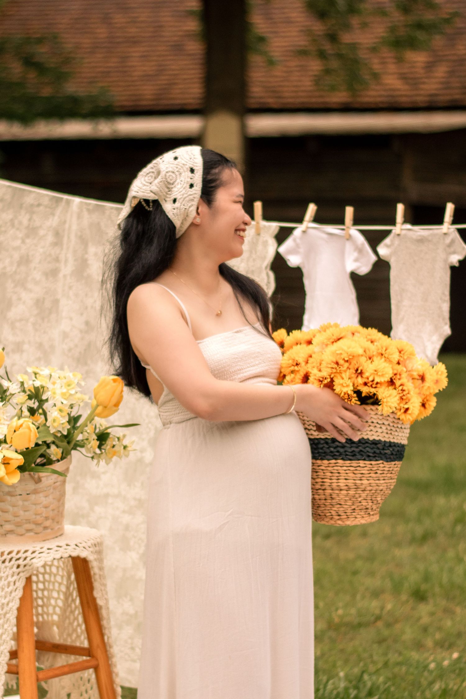 Maternity photoshoot with bright yellow sunflowers and white linens hanging in an outdoor garden setting.