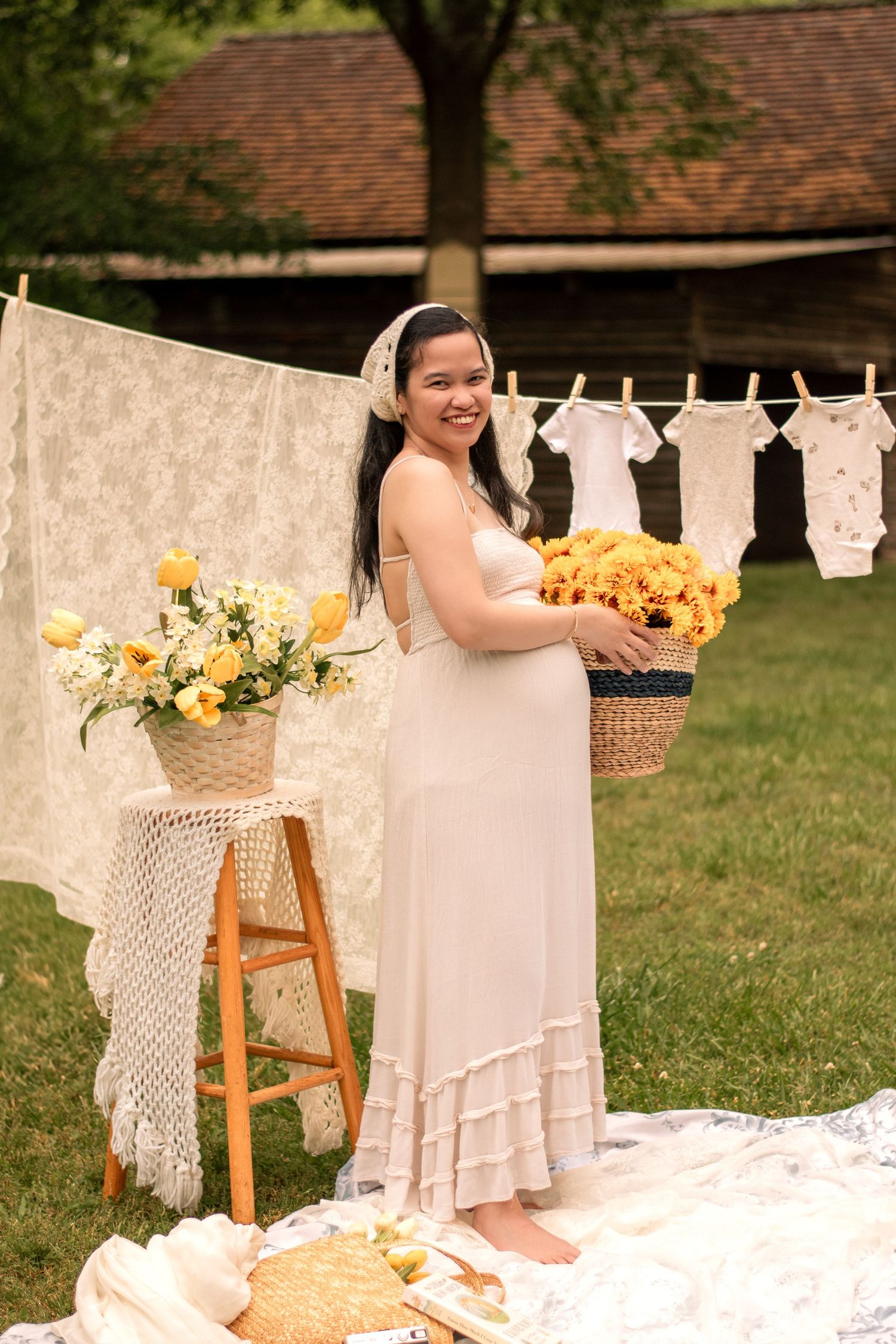 Outdoor maternity scene with sunflowers and white linens on clothesline against brick building backdrop.