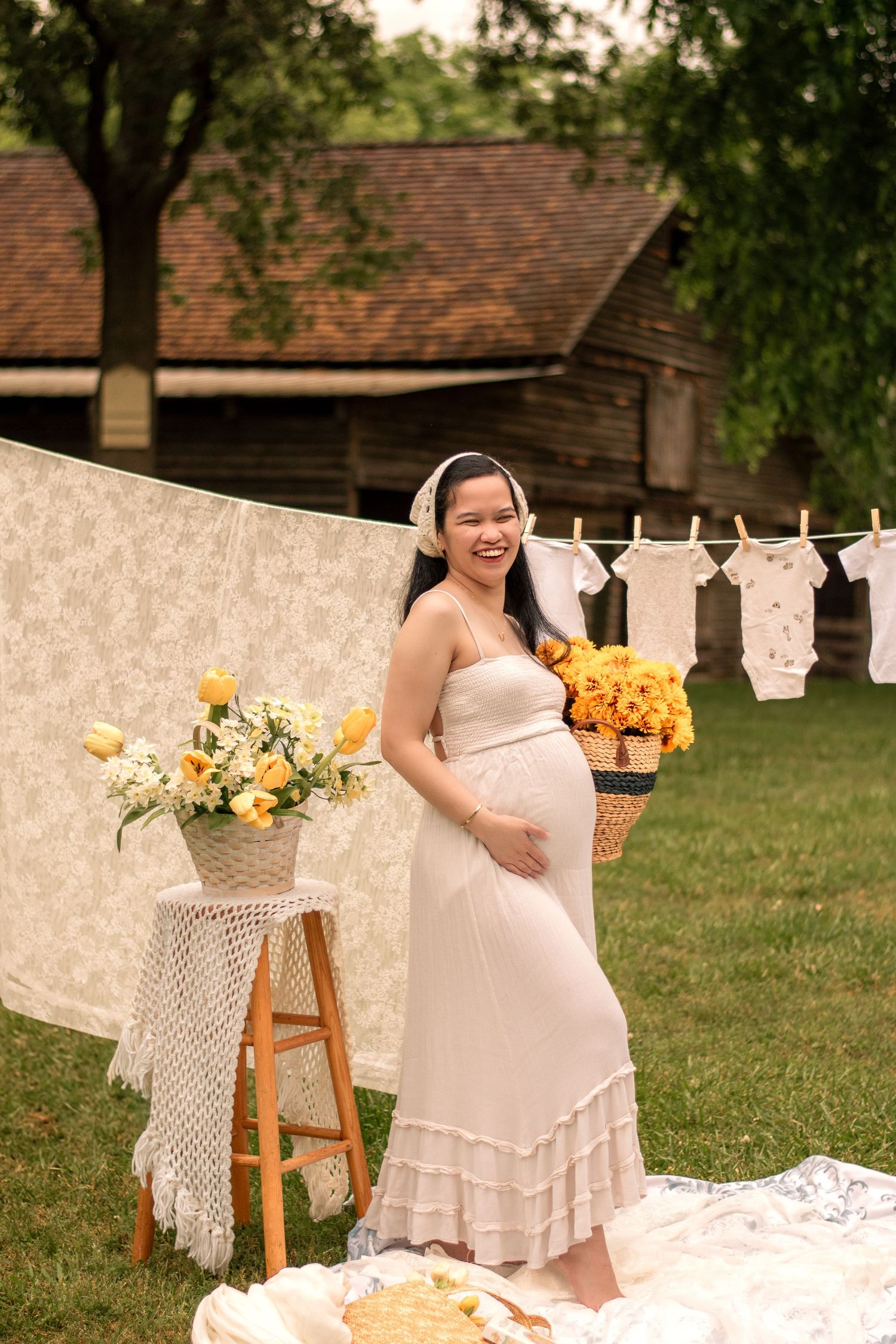 Garden maternity session with wooden stool, hanging linens, and yellow flower arrangements.