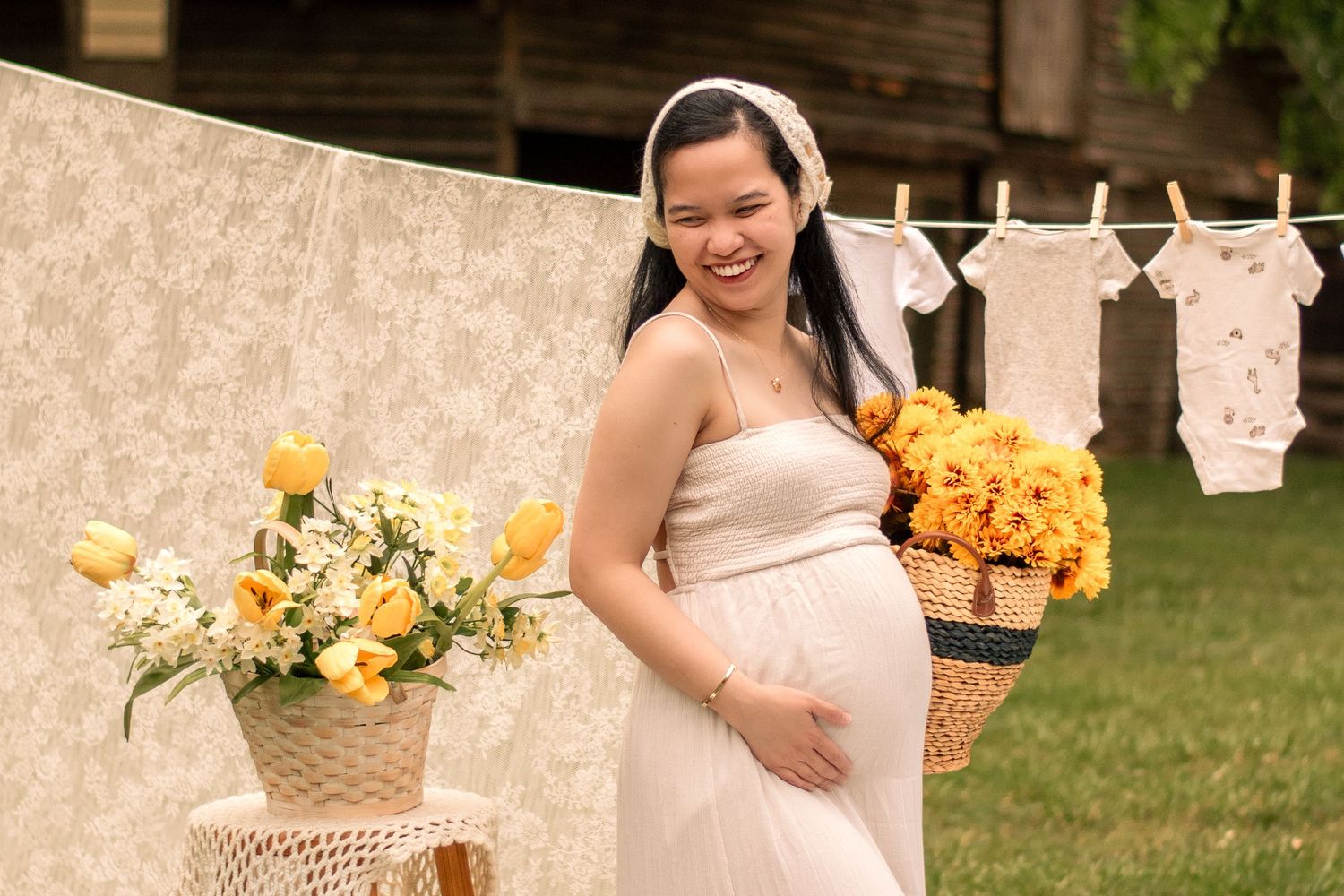 Elegant maternity photography setup with yellow flowers and white fabric decorations outdoors.