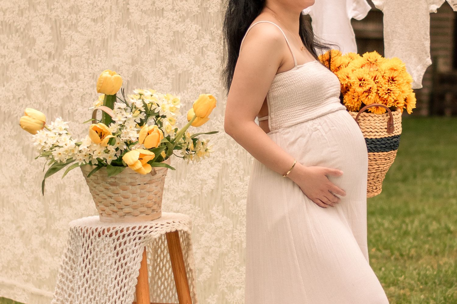Rustic maternity photo session featuring yellow bouquets and white lace backdrop in garden setting.