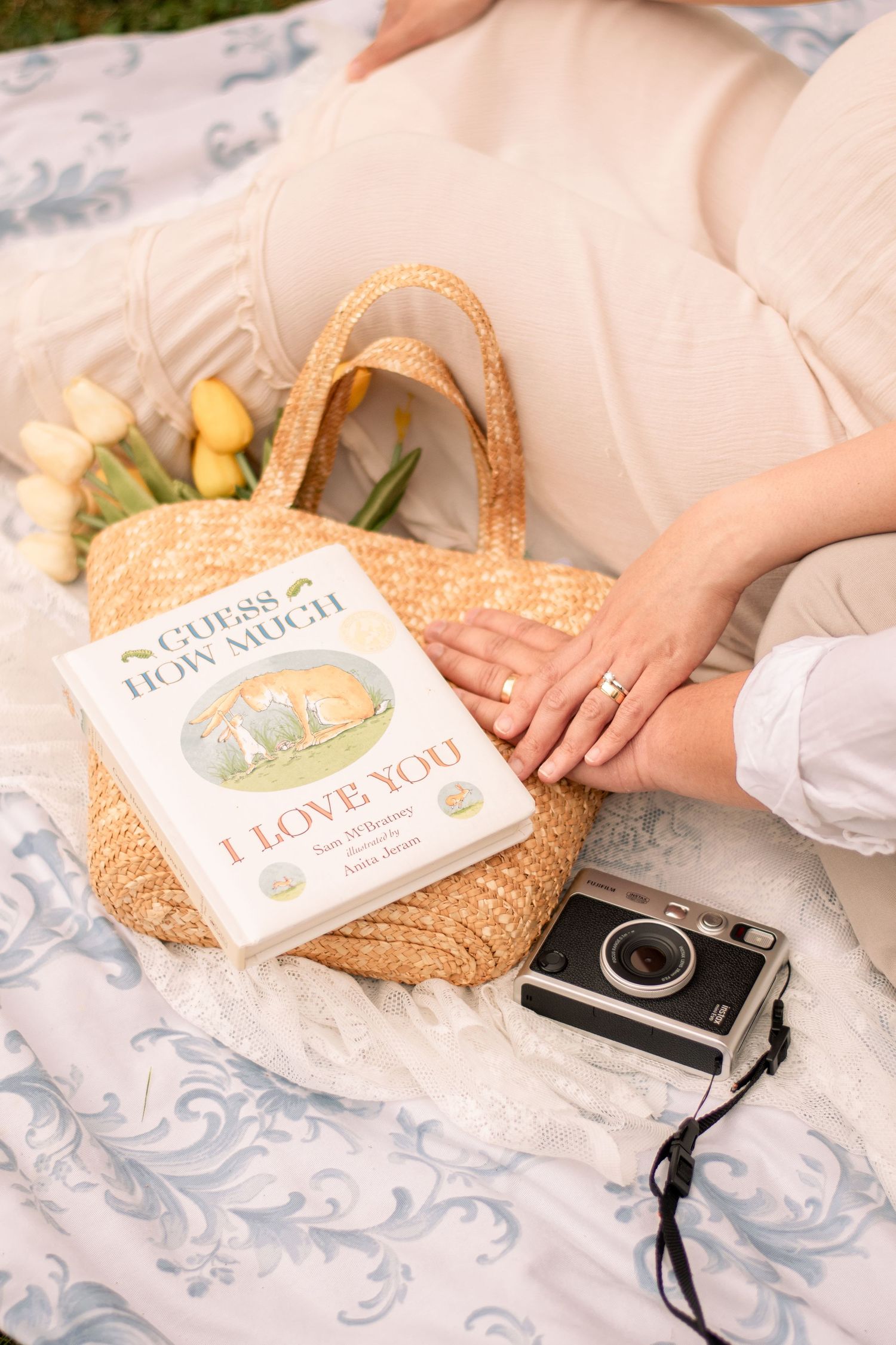 Vintage camera and children's books arranged on lace blanket during outdoor photoshoot.