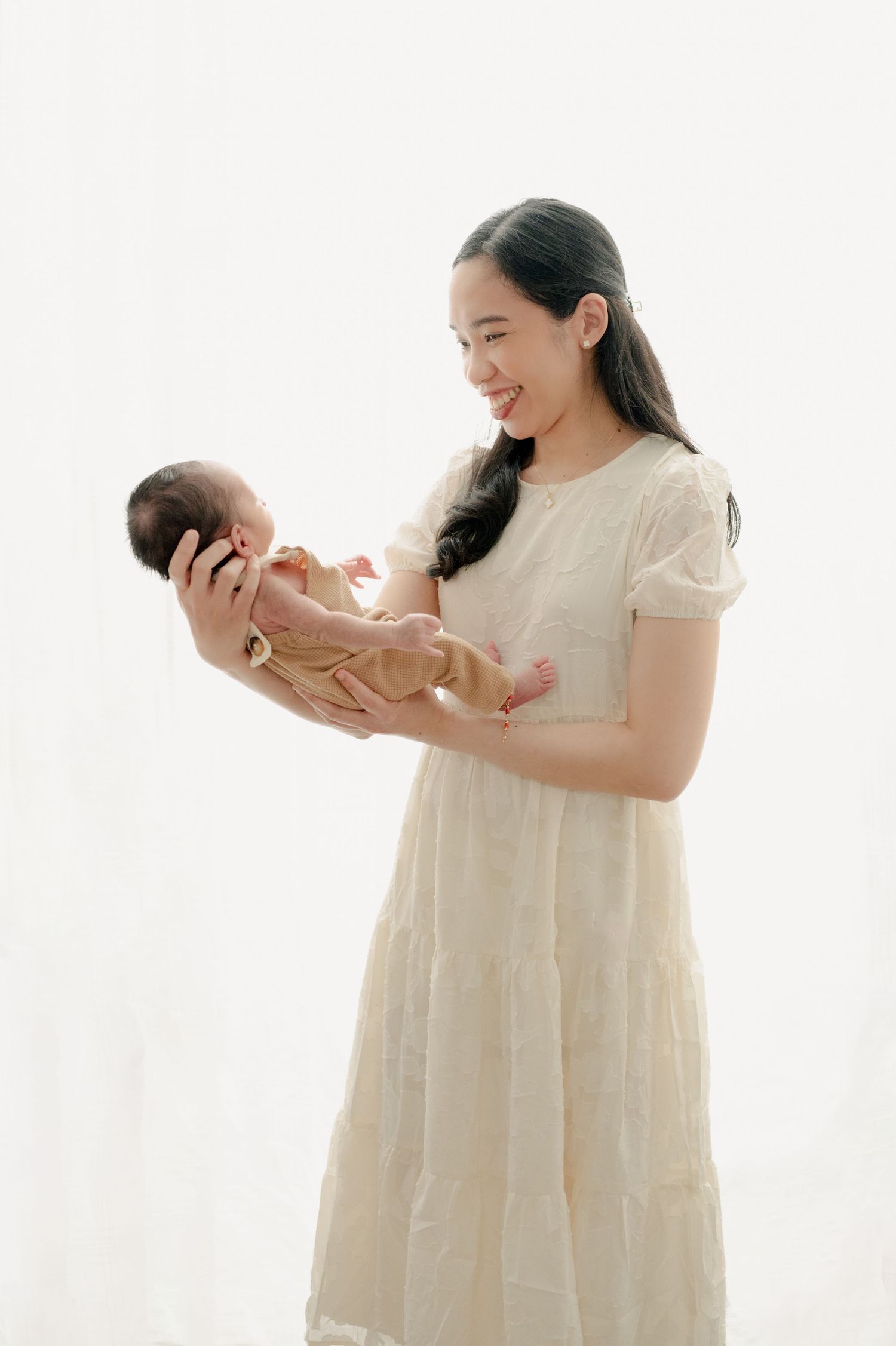 Mother in cream dress holding newborn baby against white background.