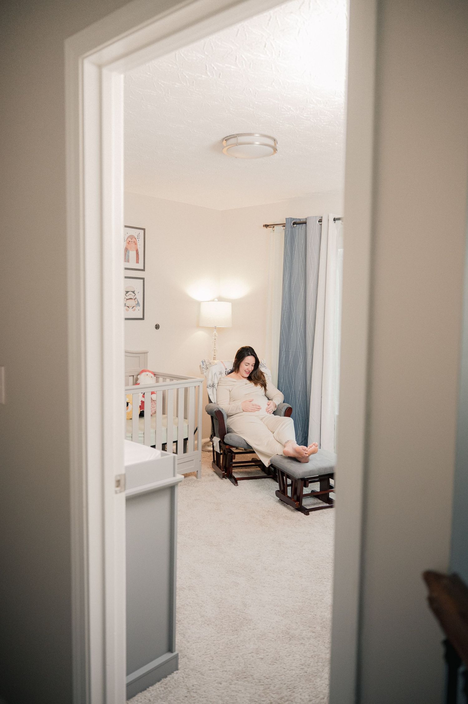 View through doorway of a bright nursery with rocking chair and blue curtains.