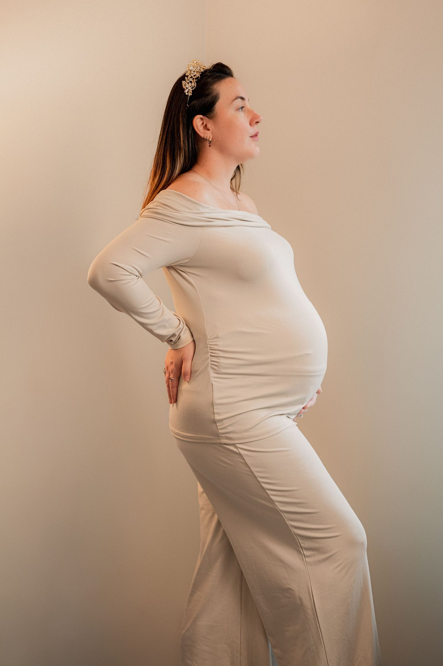 Maternity photoshoot featuring poses in a cream-colored dress against a neutral background.