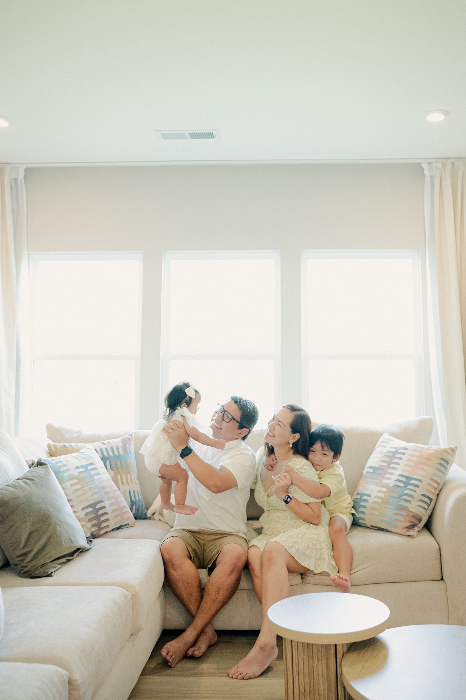 Family lounging together on a large white sectional sofa in a sun-filled living room.