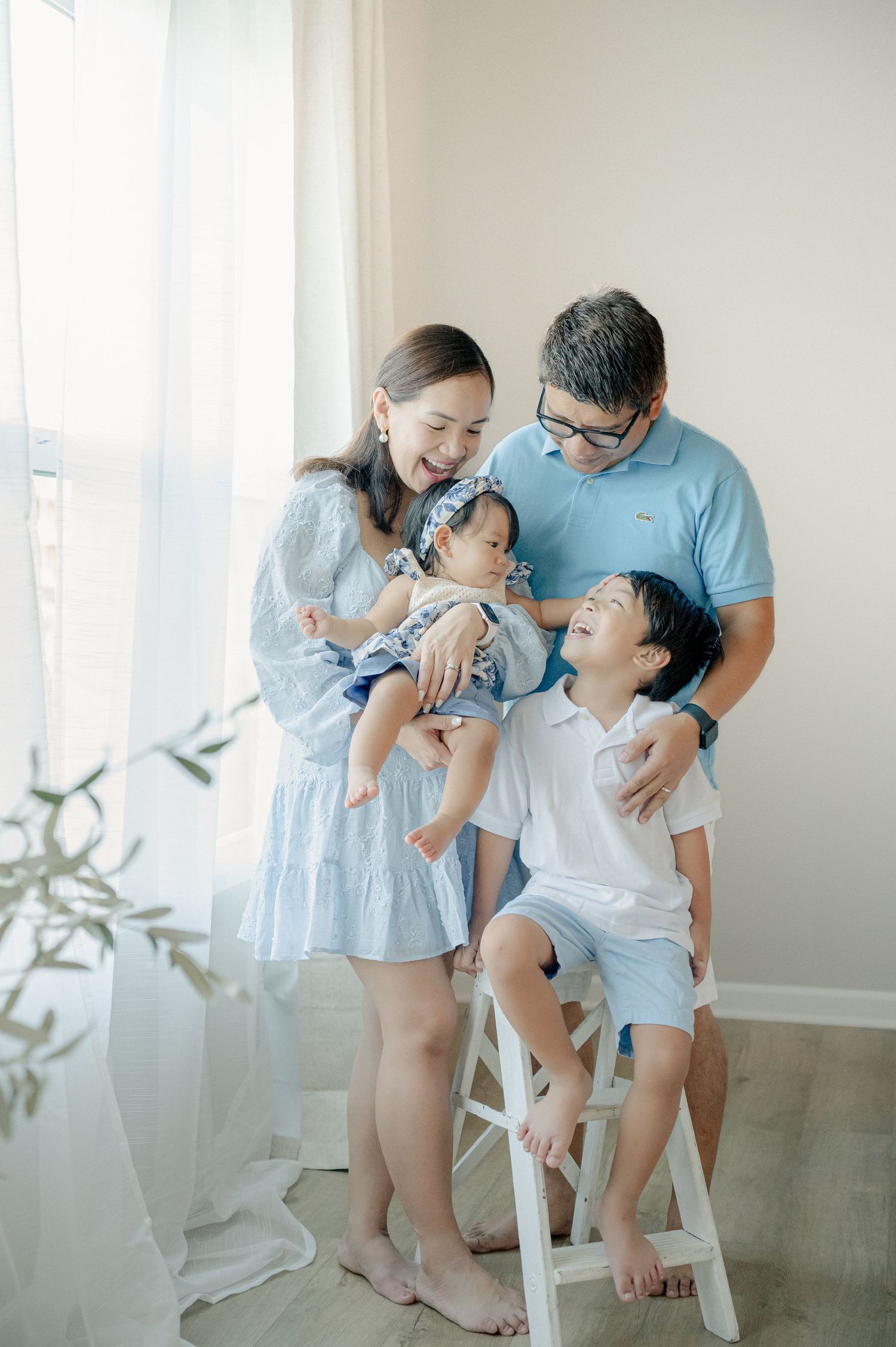 Family wearing coordinated blue and white outfits sharing tender moments in a bright room.