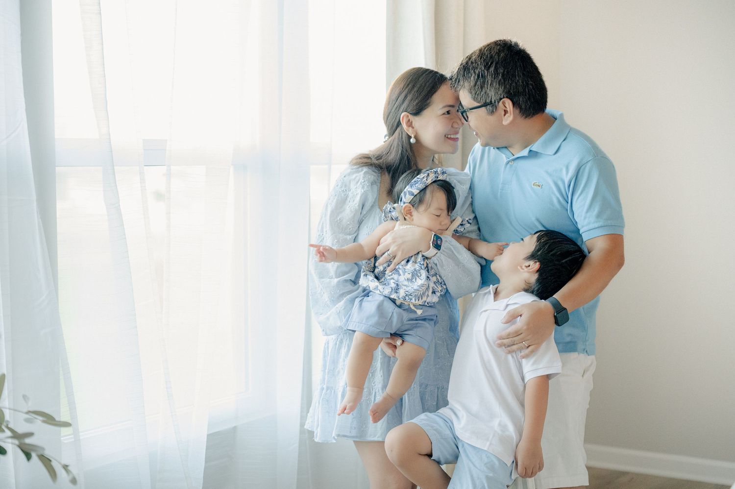 Family wearing coordinated blue and white outfits sharing tender moments in a bright sunlit room.