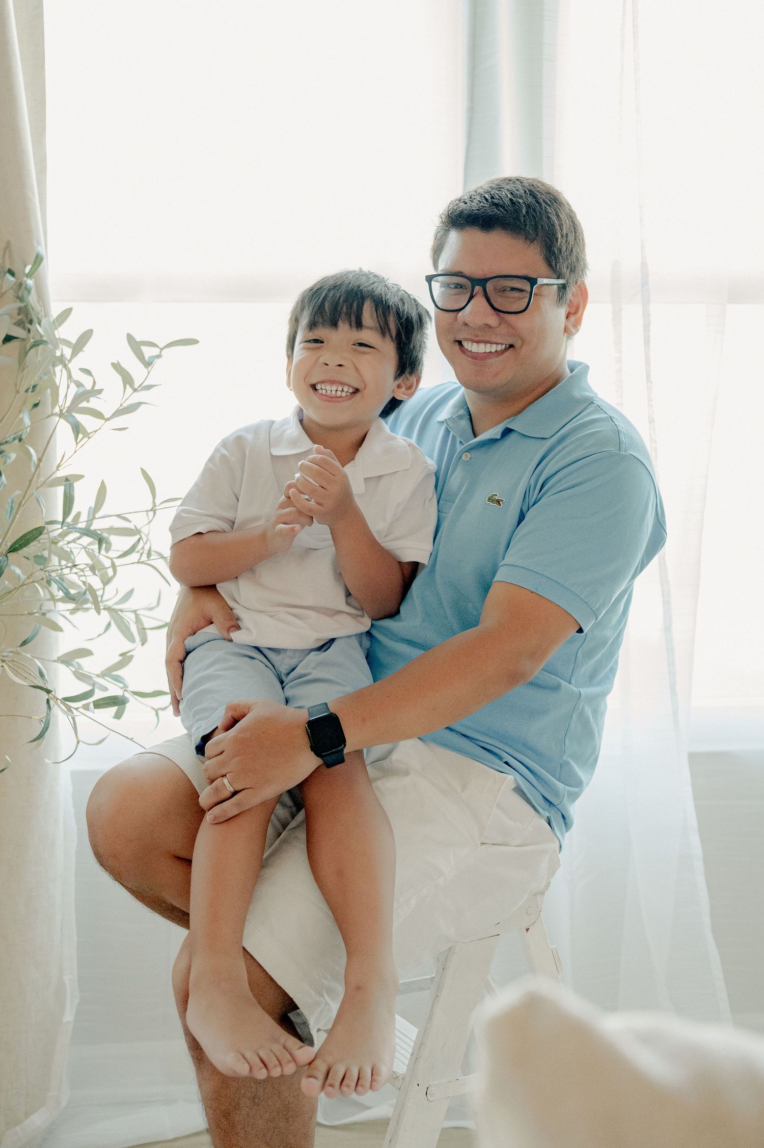 Family sharing laughs while sitting together on white furniture near window.