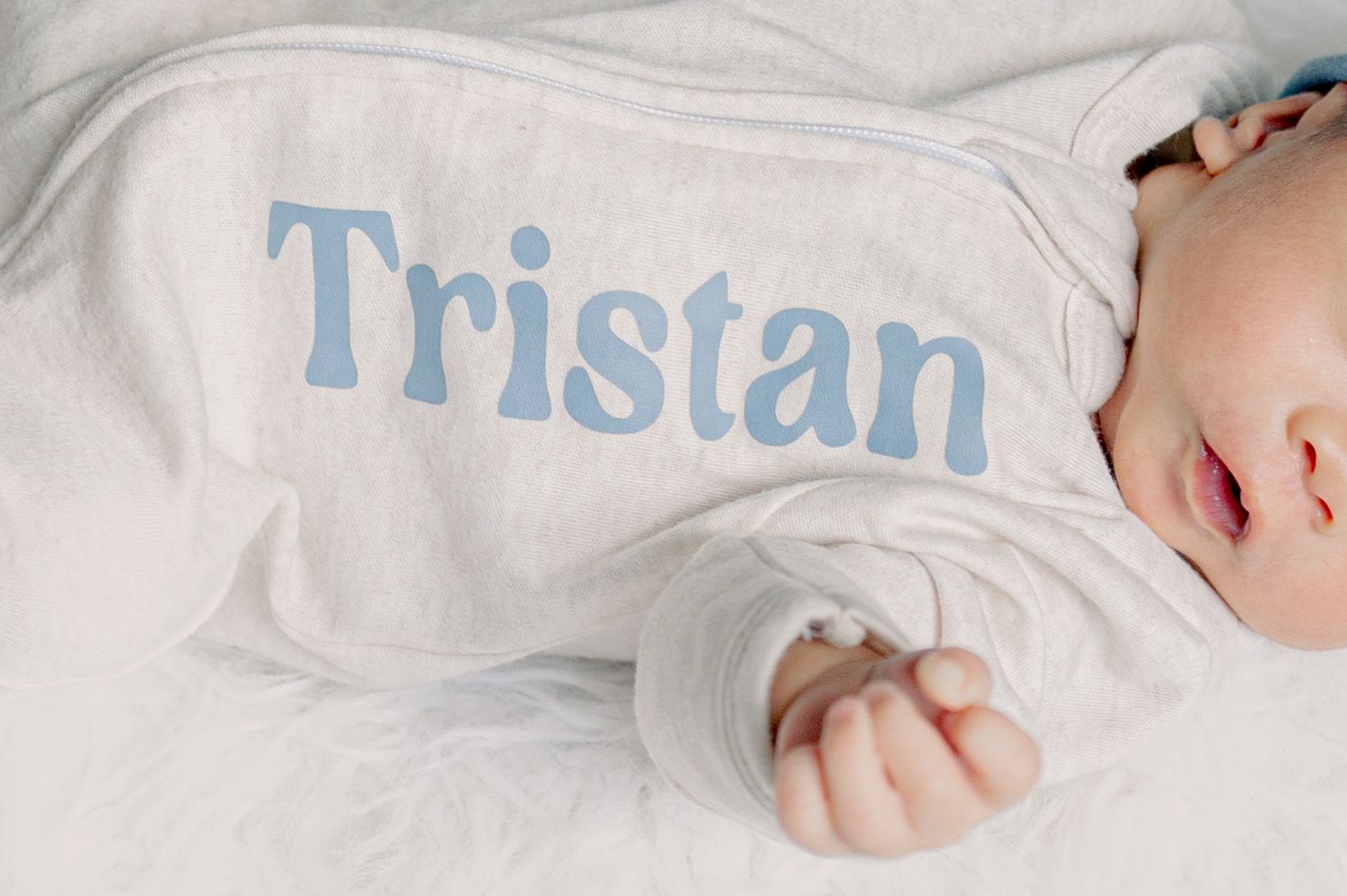 Sleeping baby wrapped in white blanket with name 'Tristan' embroidered in blue letters.