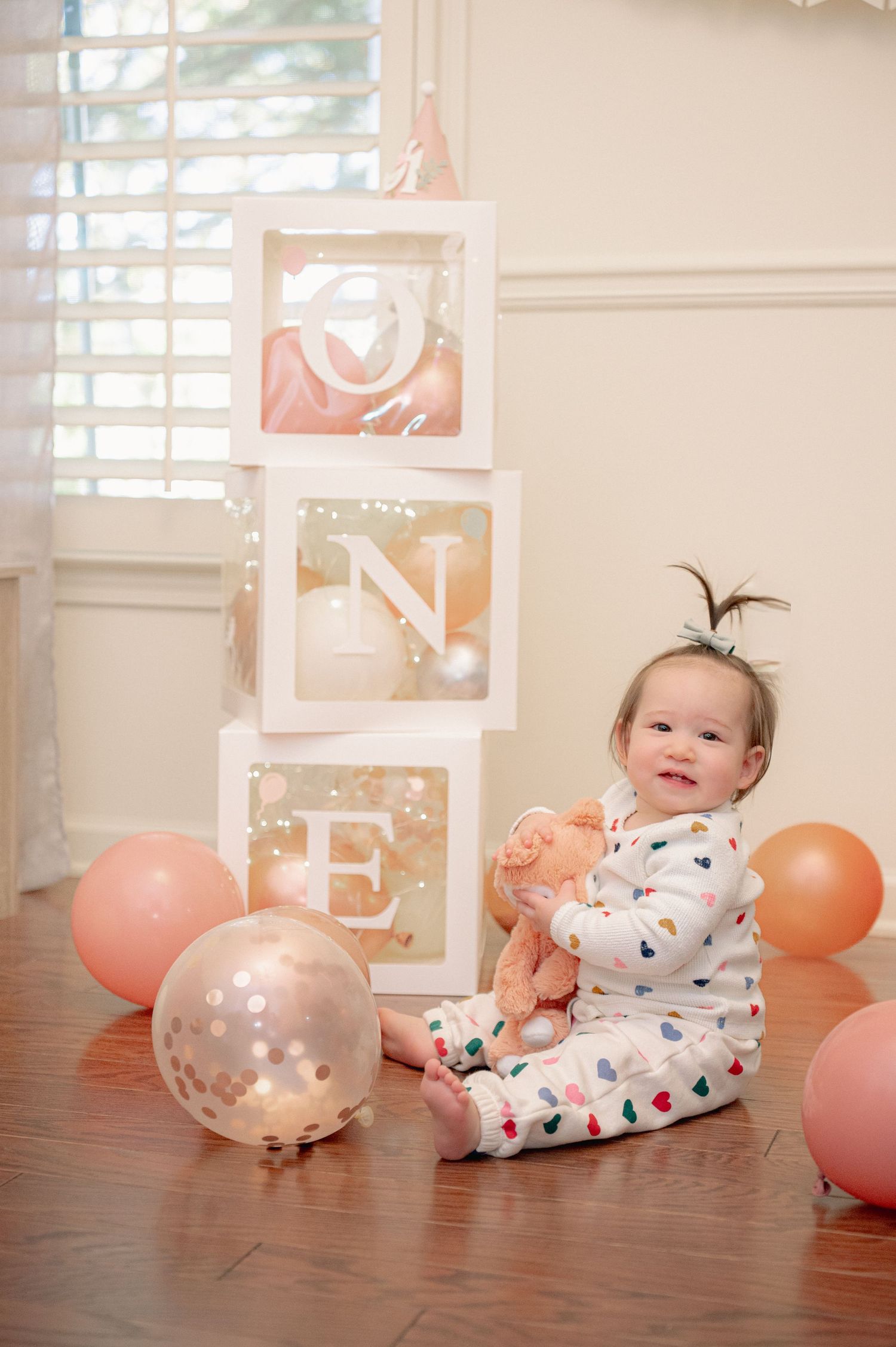 Festive birthday setup with balloons, decorations and baby on hardwood floor.