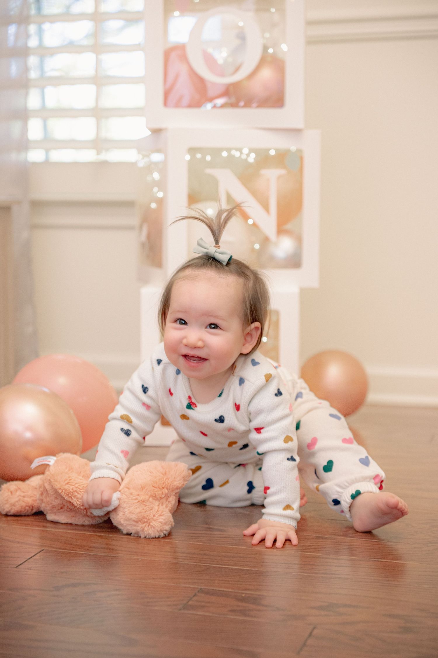 Baby crawling on hardwood floor surrounded by pink balloons and party decorations.
