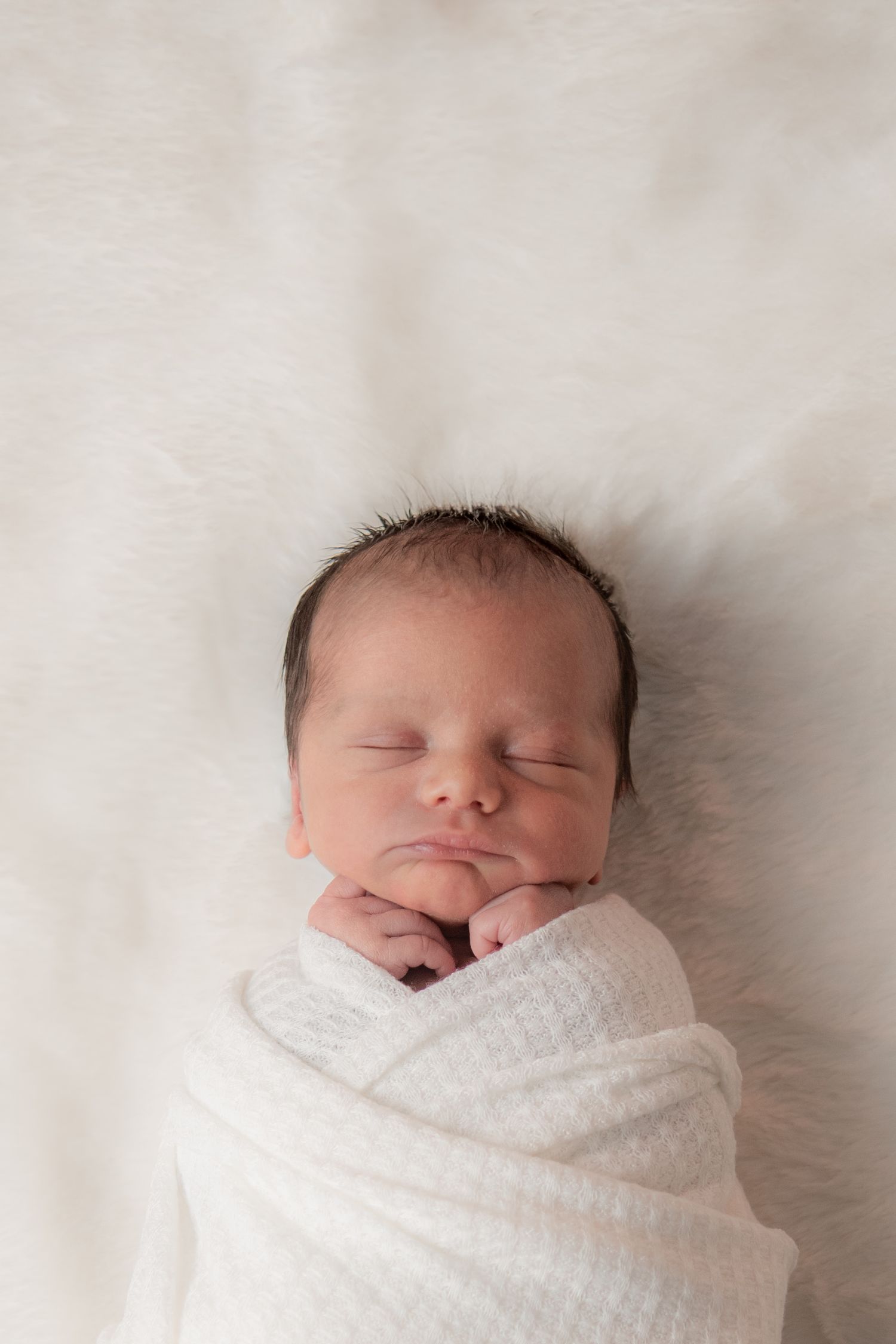 Newborn baby sleeping peacefully while swaddled in white blanket against white background.
