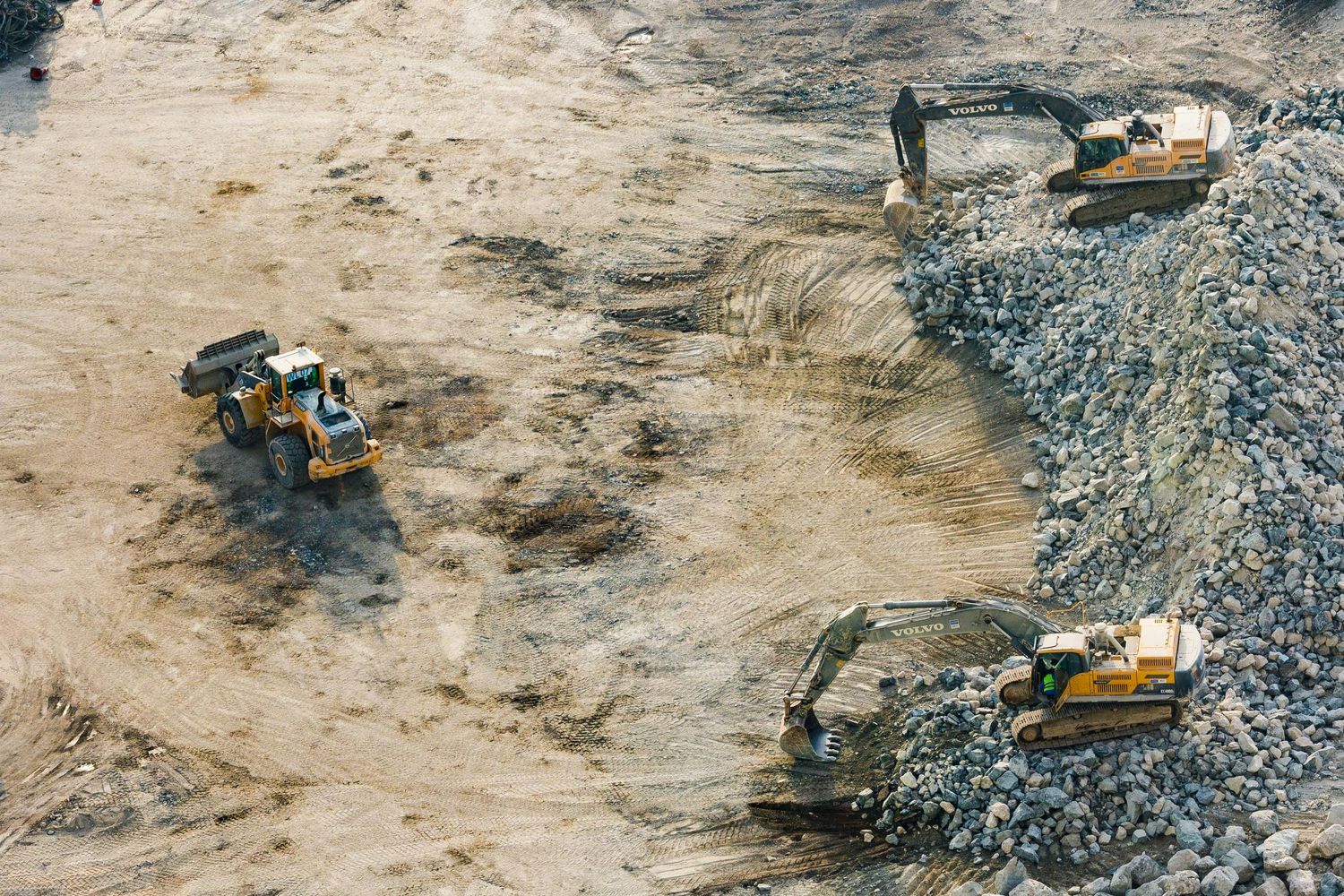 Aerial view of construction equipment working at a landfill with large piles of waste and debris.