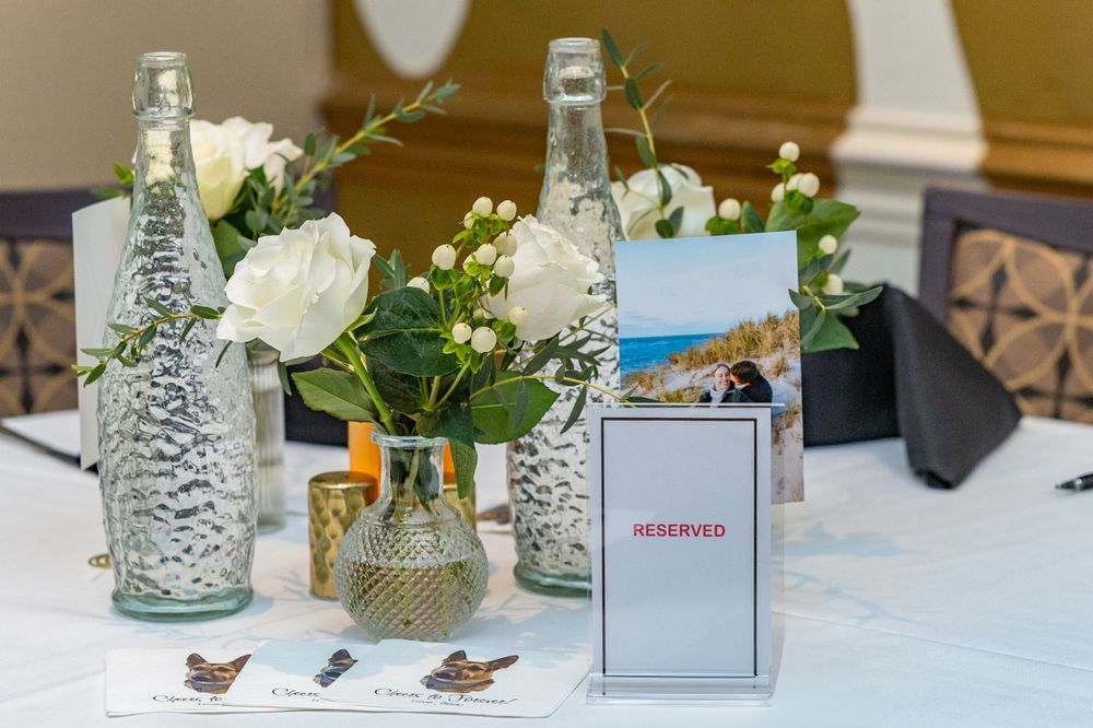 Table decor featuring white roses and greenery in glass vases with decorative cards.