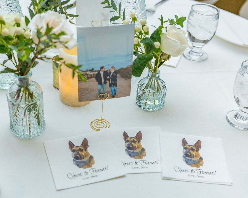 Table setting with blue glass vases, place cards featuring dog illustrations, and a photo display at a reception.