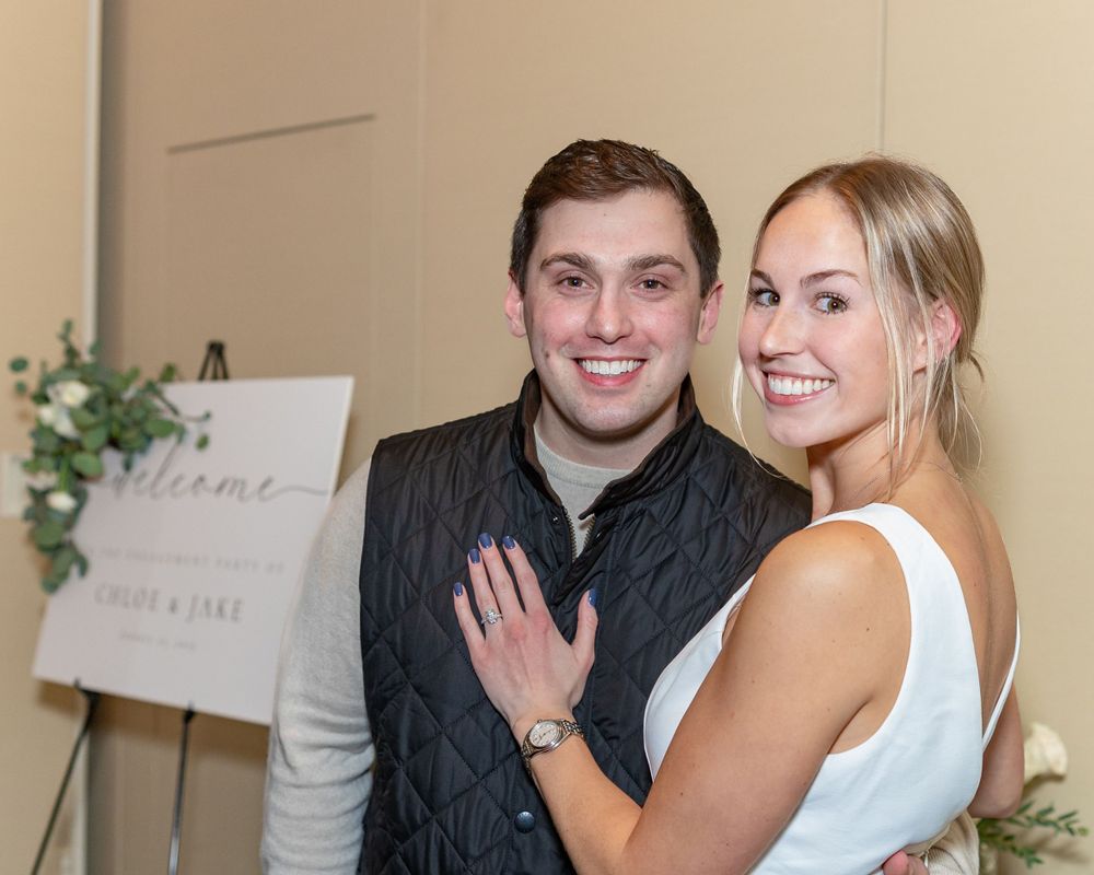 An elegant celebration pose against a beige wall with floral decorations at an engagement party at Arturo's restaurant in Westborough, MA.