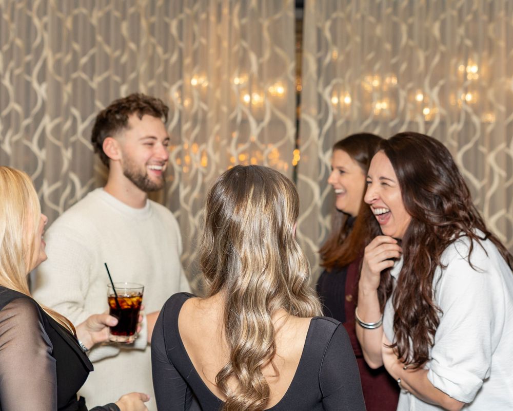Group of party guests laughing and socializing at an indoor event with decorative lighting during engagement party in Westborough, MA.