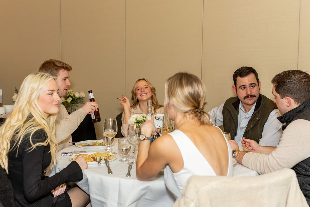 Engagement party guests engaged in lively conversation around a dinner table  during engagement party in Westborough, MA.  Event Photography