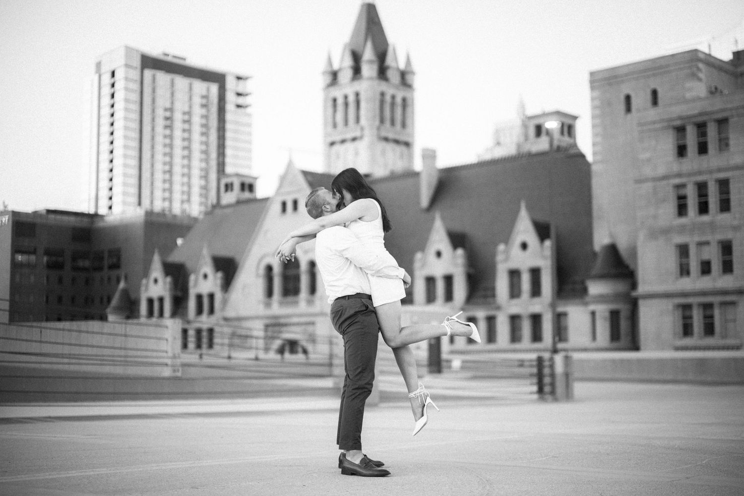 A couple embraces in a romantic dance pose on a rooftop with historic architecture and a church steeple in the background.