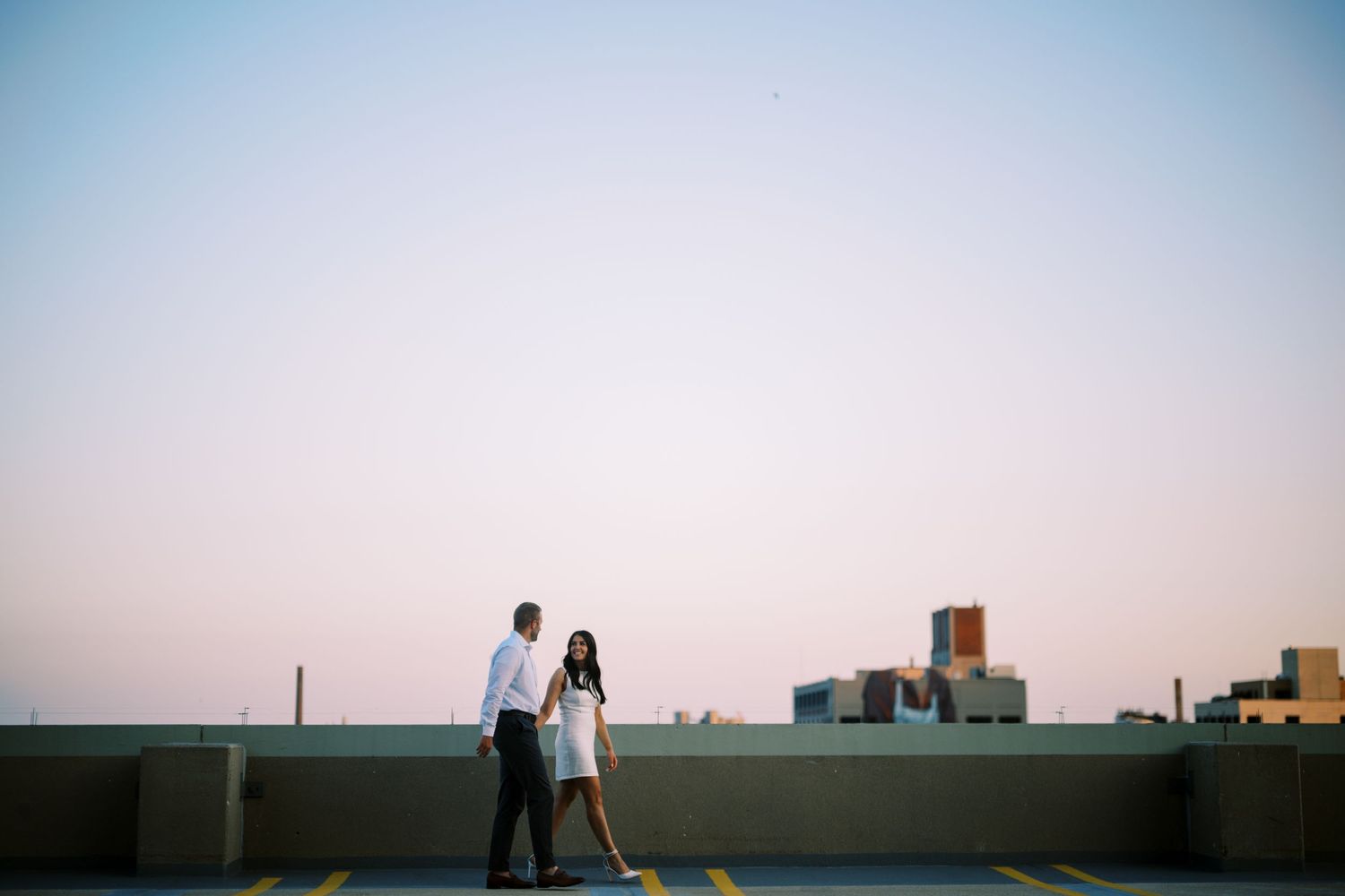 Two people standing together on a rooftop against a city skyline at dusk.