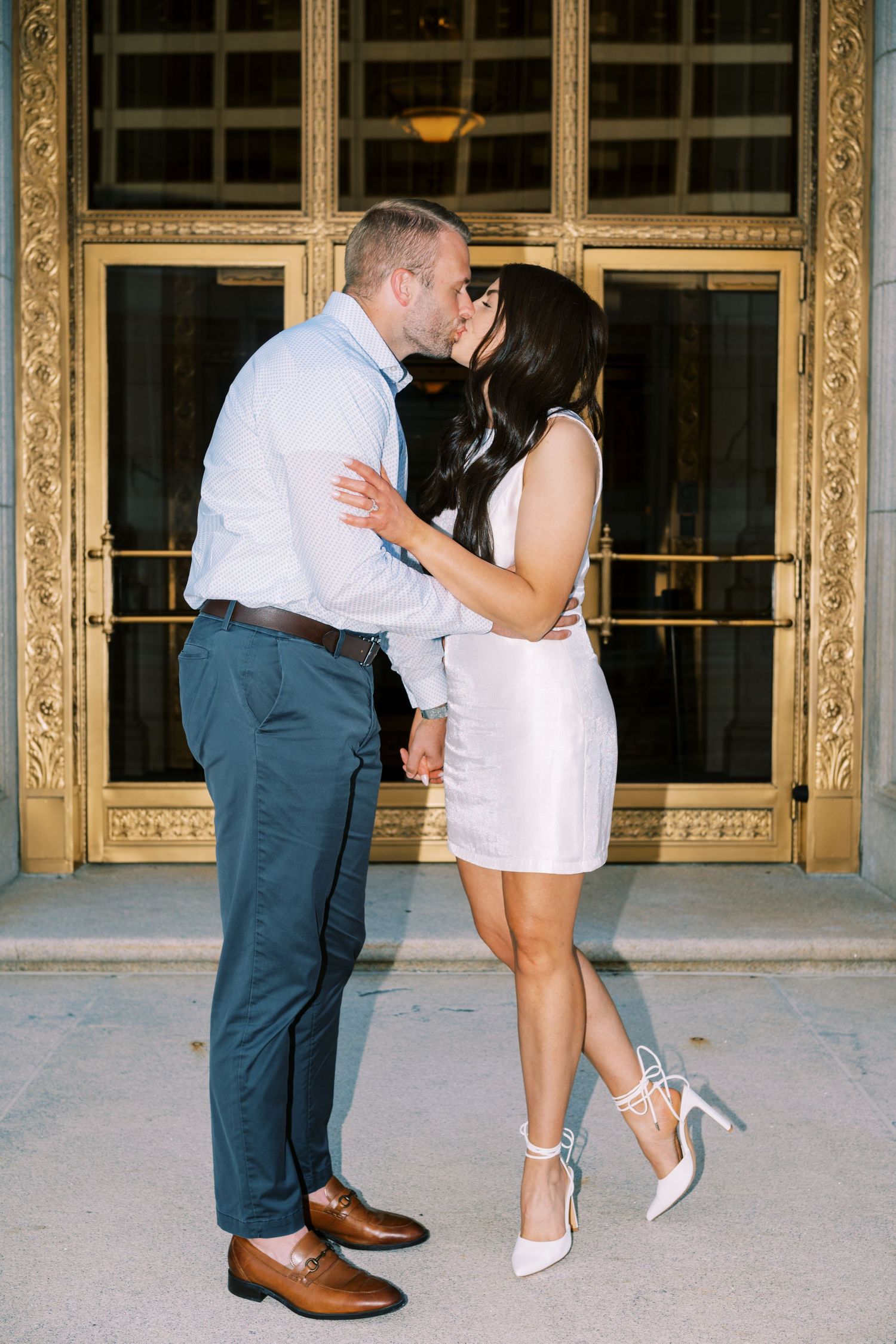A romantic couple shares an intimate moment in front of an elegant gold-framed doorway.