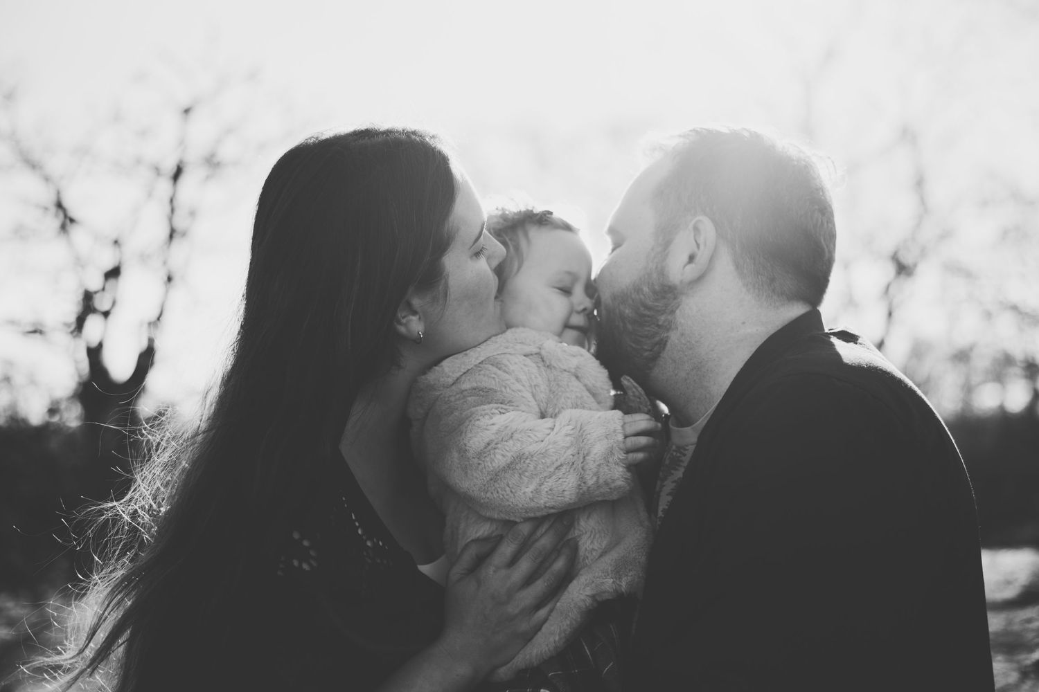 Tender family moment captured in silhouette against bright sunlight.