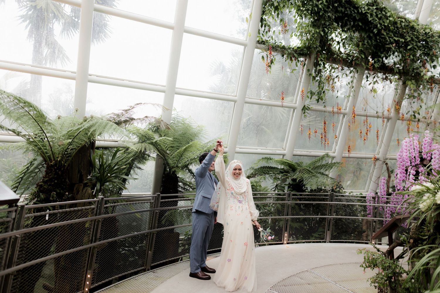 A couple in white traditional attire stands in a minimalist concrete tunnel.