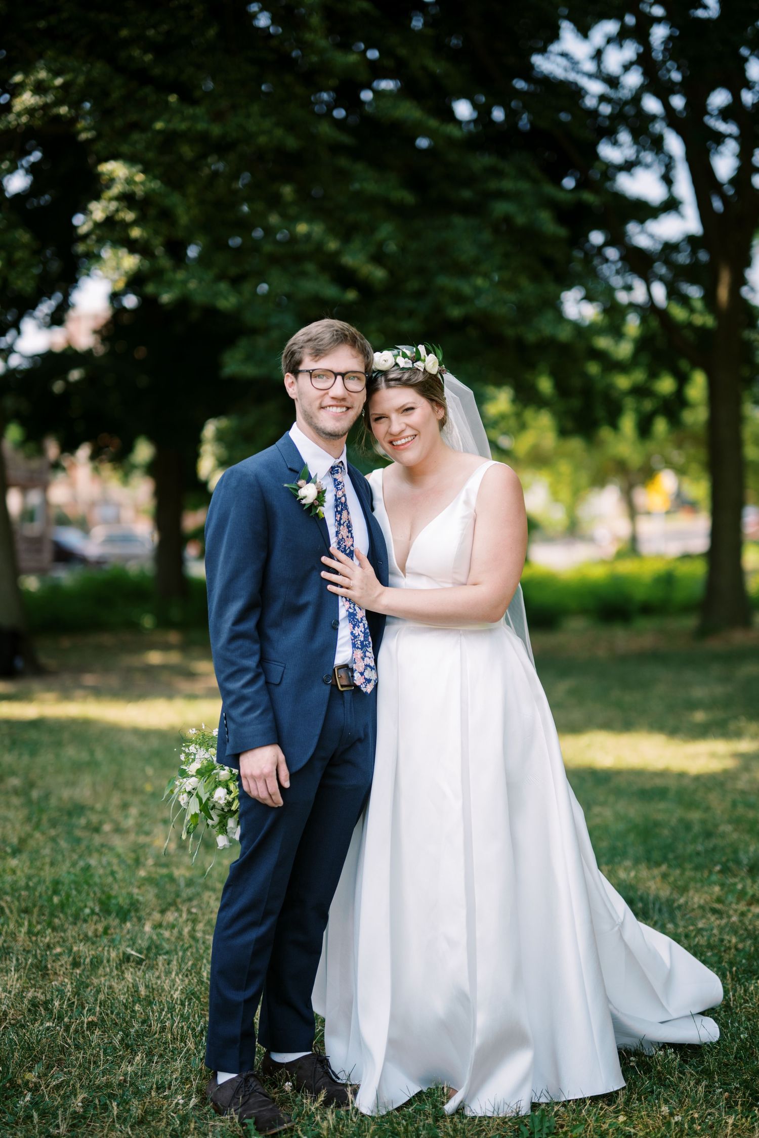 A romantic outdoor wedding portrait showing a couple in traditional wedding attire standing together on a sunlit lawn.