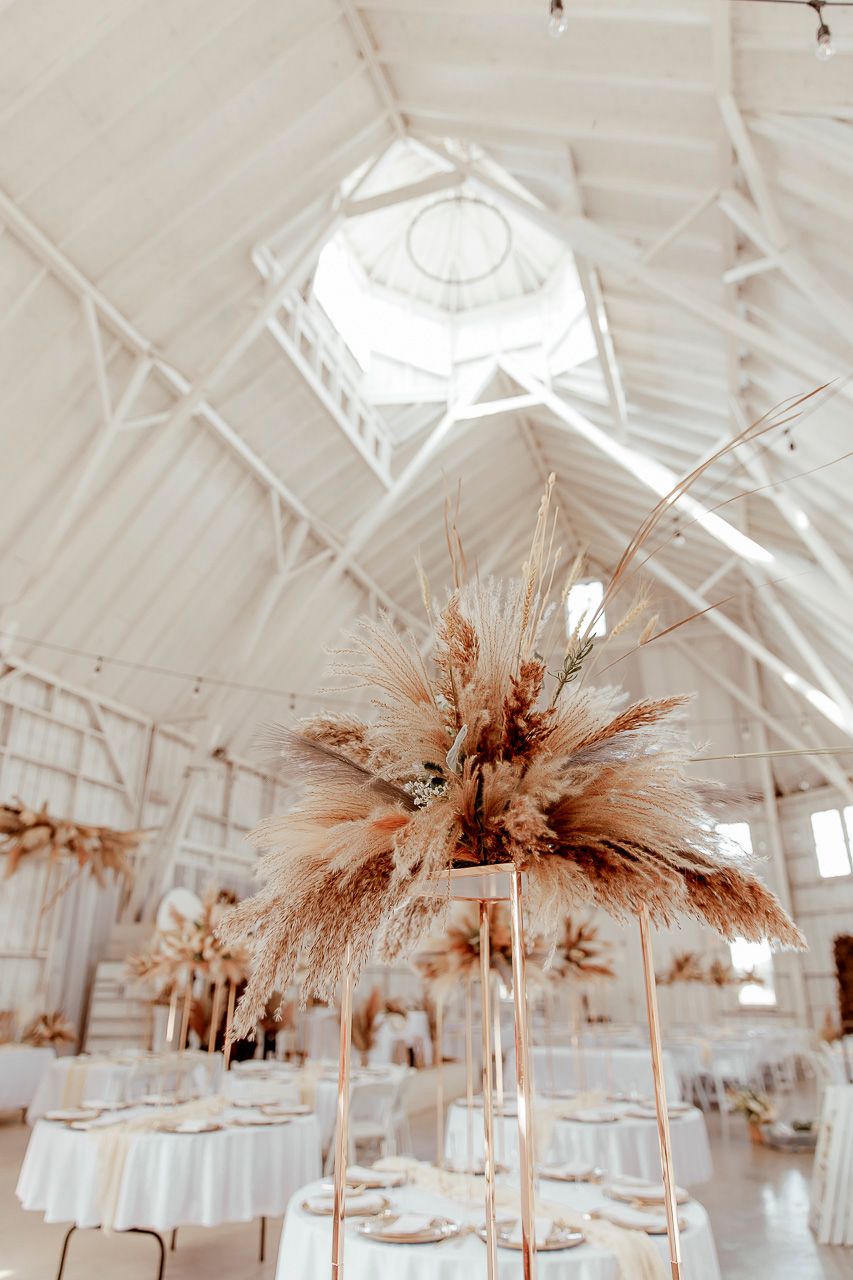 Elegant wedding venue with white vaulted ceilings and pampas grass centerpiece arrangements on round tables.